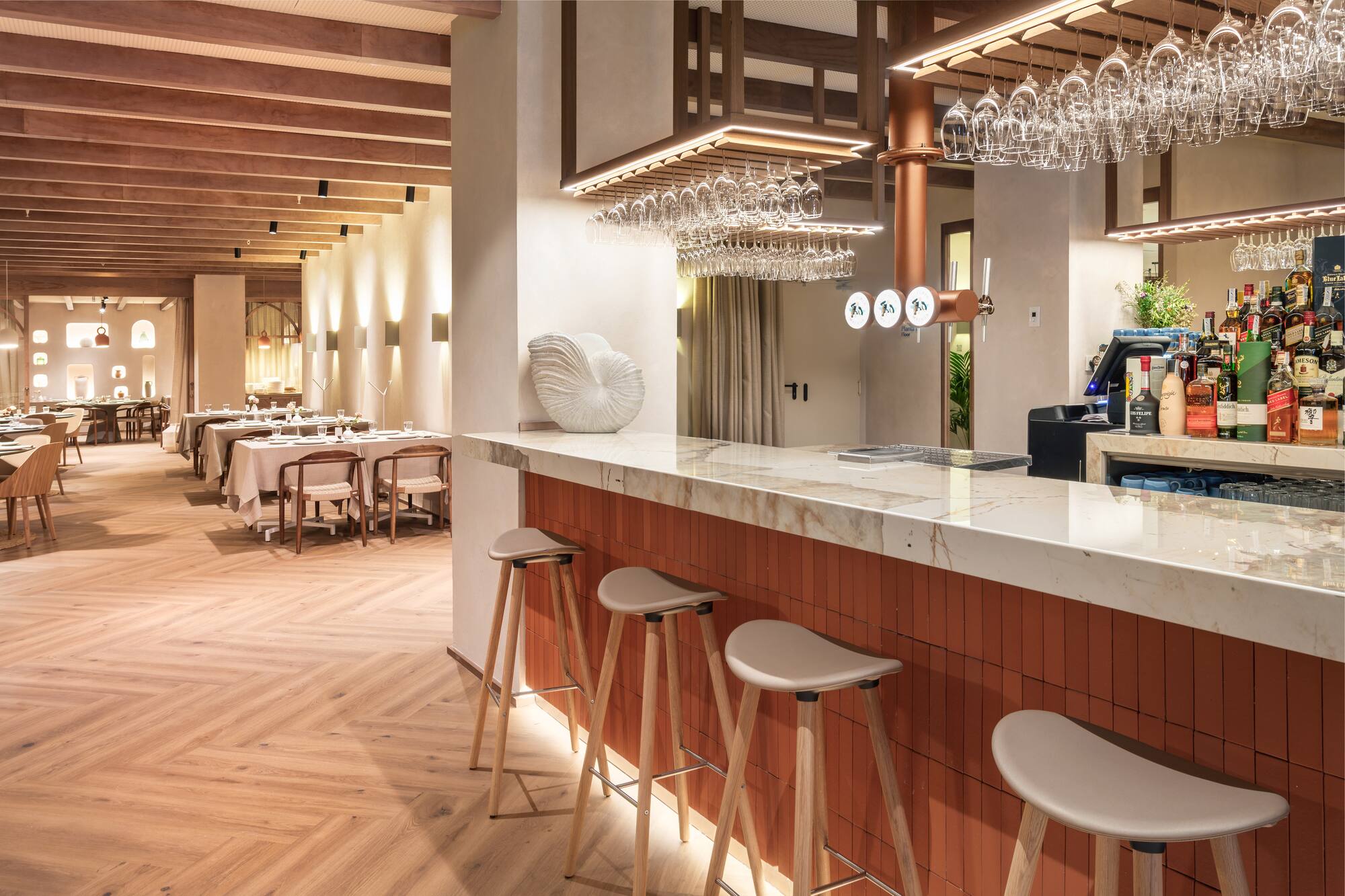 Modern restaurant interior with elegant bar, marble counter, wood accents, and dining area.