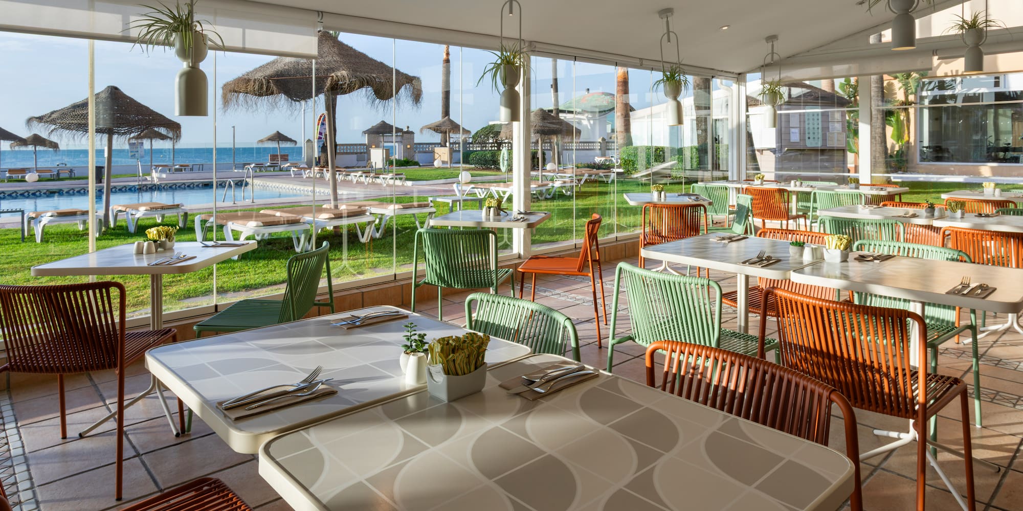 Resort restaurant with colorful chairs, pool, and sea view.