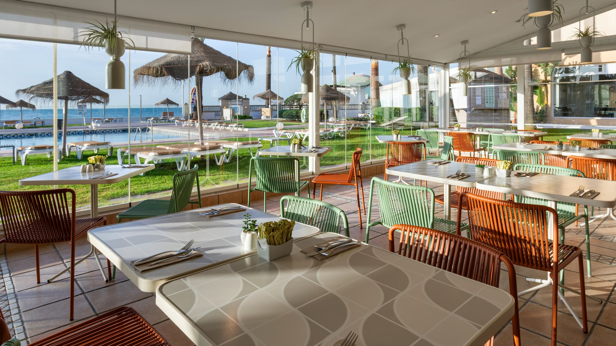 Resort restaurant with colorful chairs, pool, and sea view.
