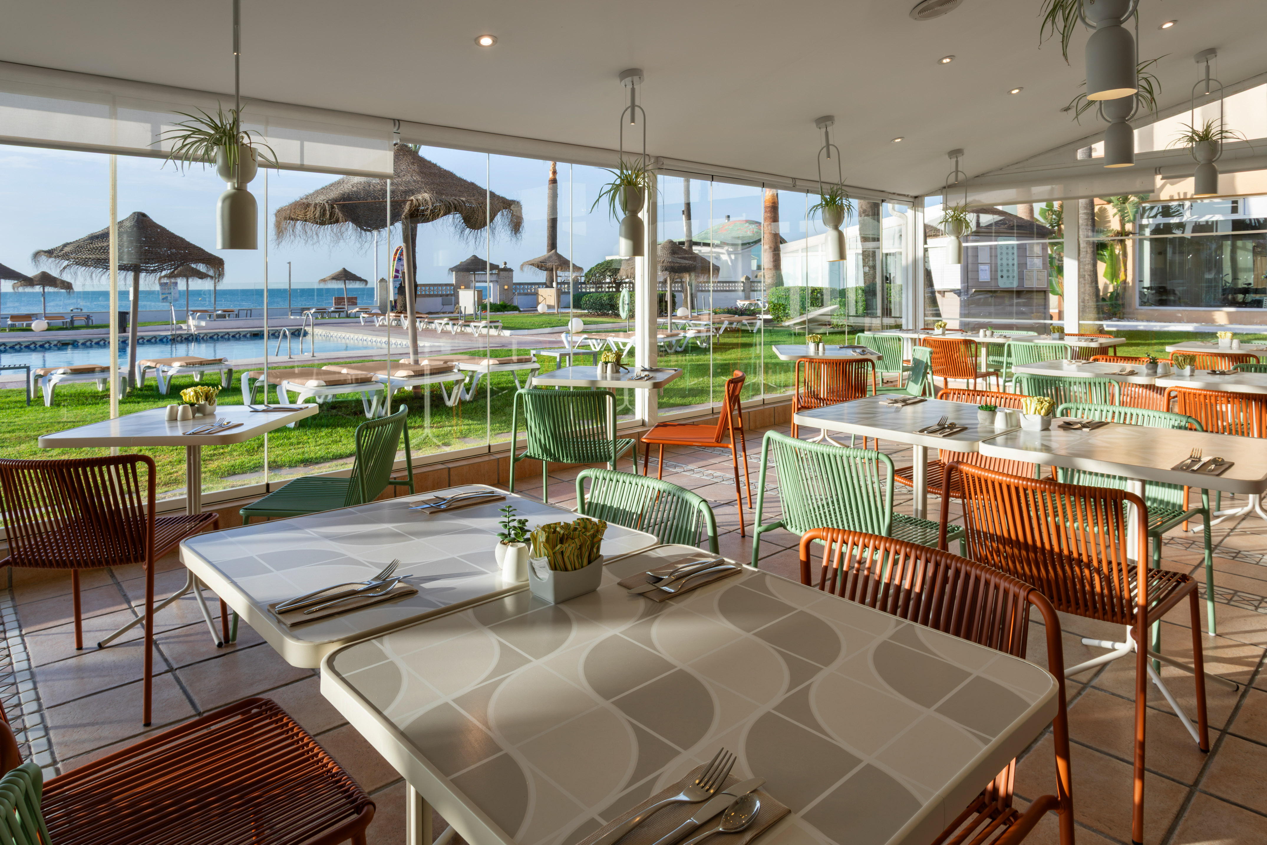 Resort restaurant with colorful chairs, pool, and sea view.