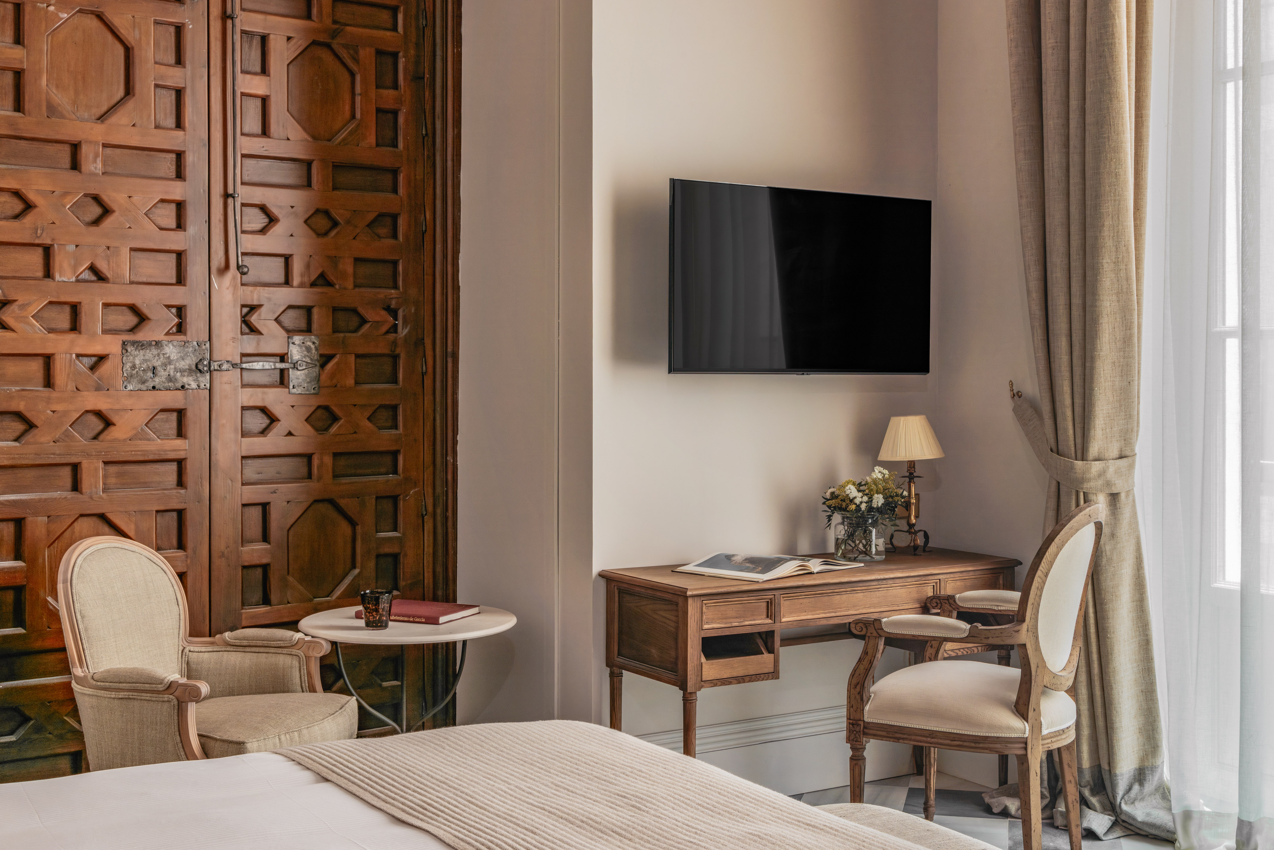 Stylish hotel bedroom featuring traditional carved wooden doors, desk, and TV.