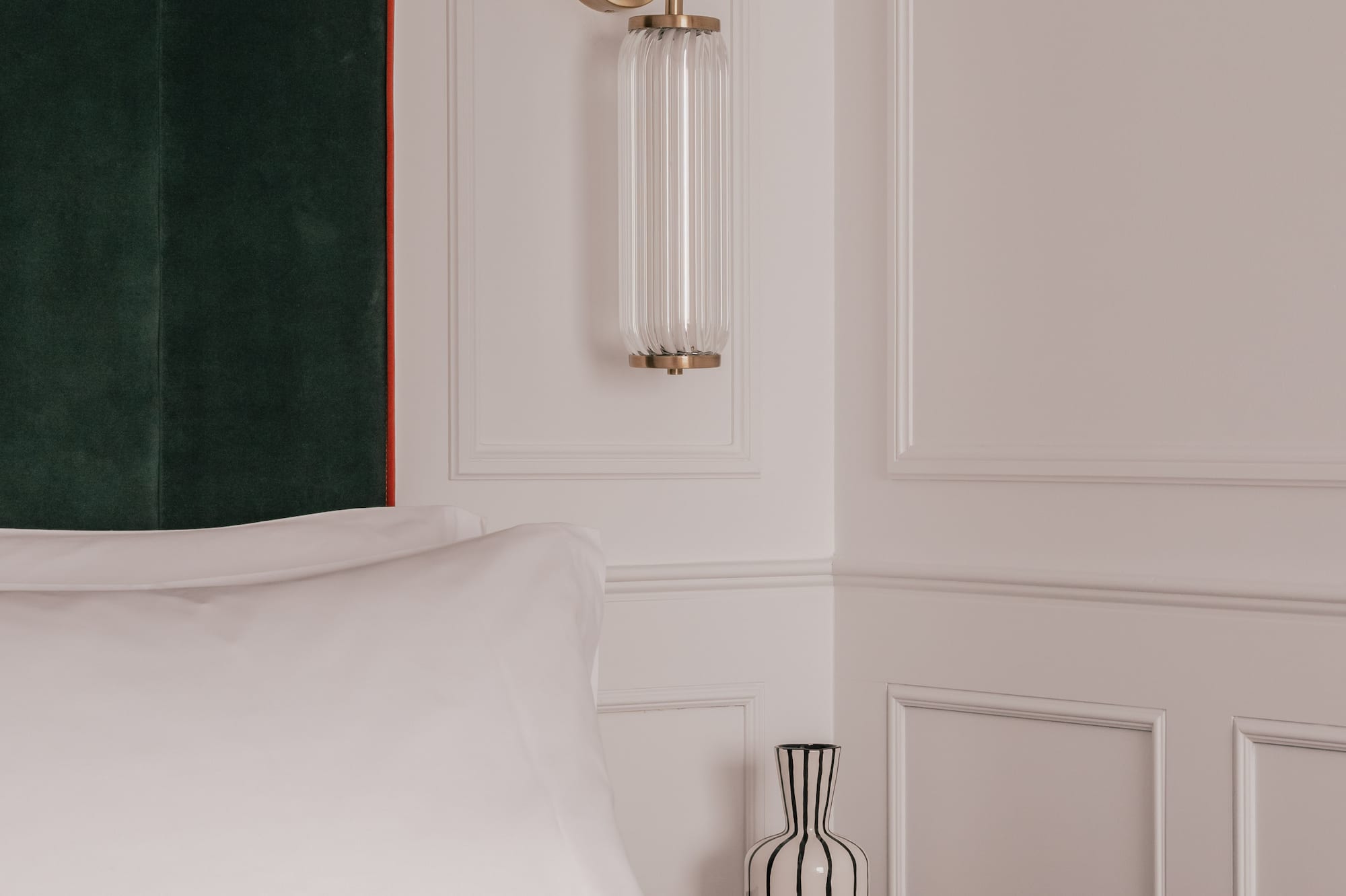Modern bedroom: green velvet headboard, brass wall sconce, striped vase.