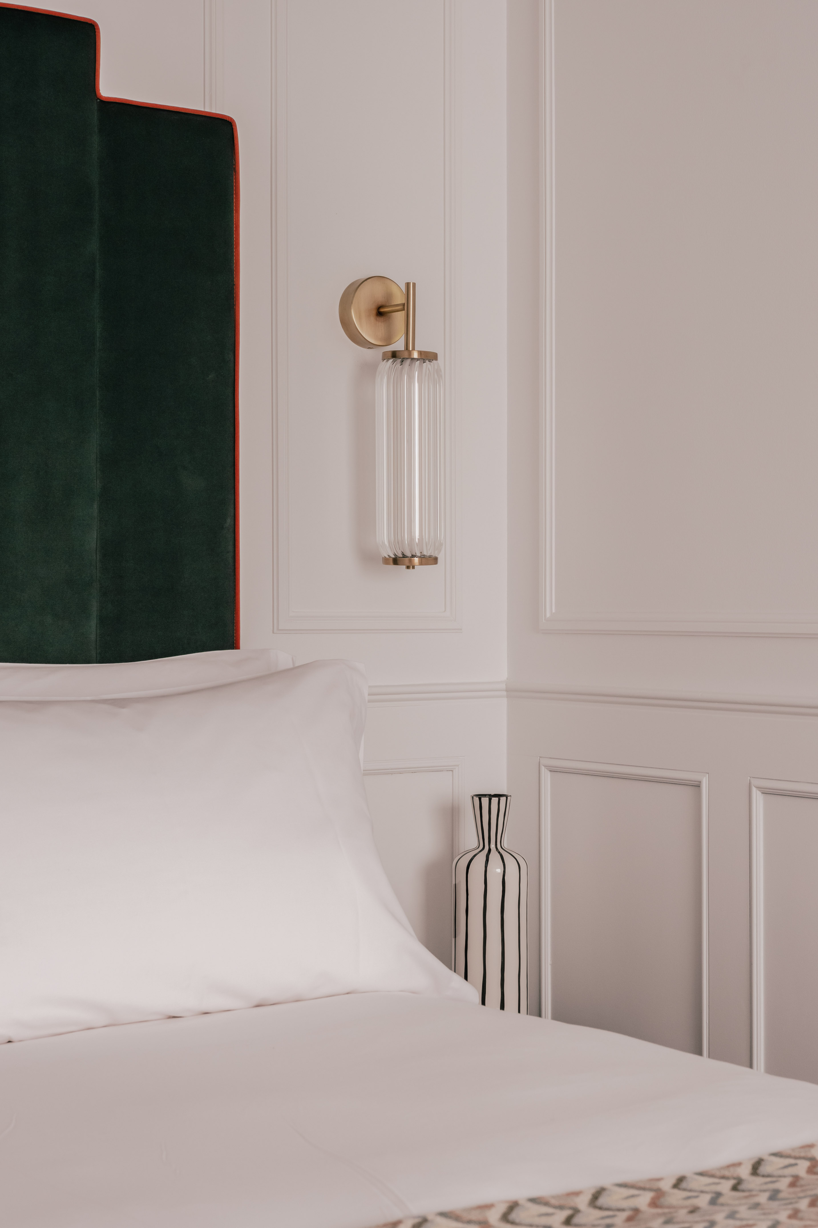 Modern bedroom: green velvet headboard, brass wall sconce, striped vase.