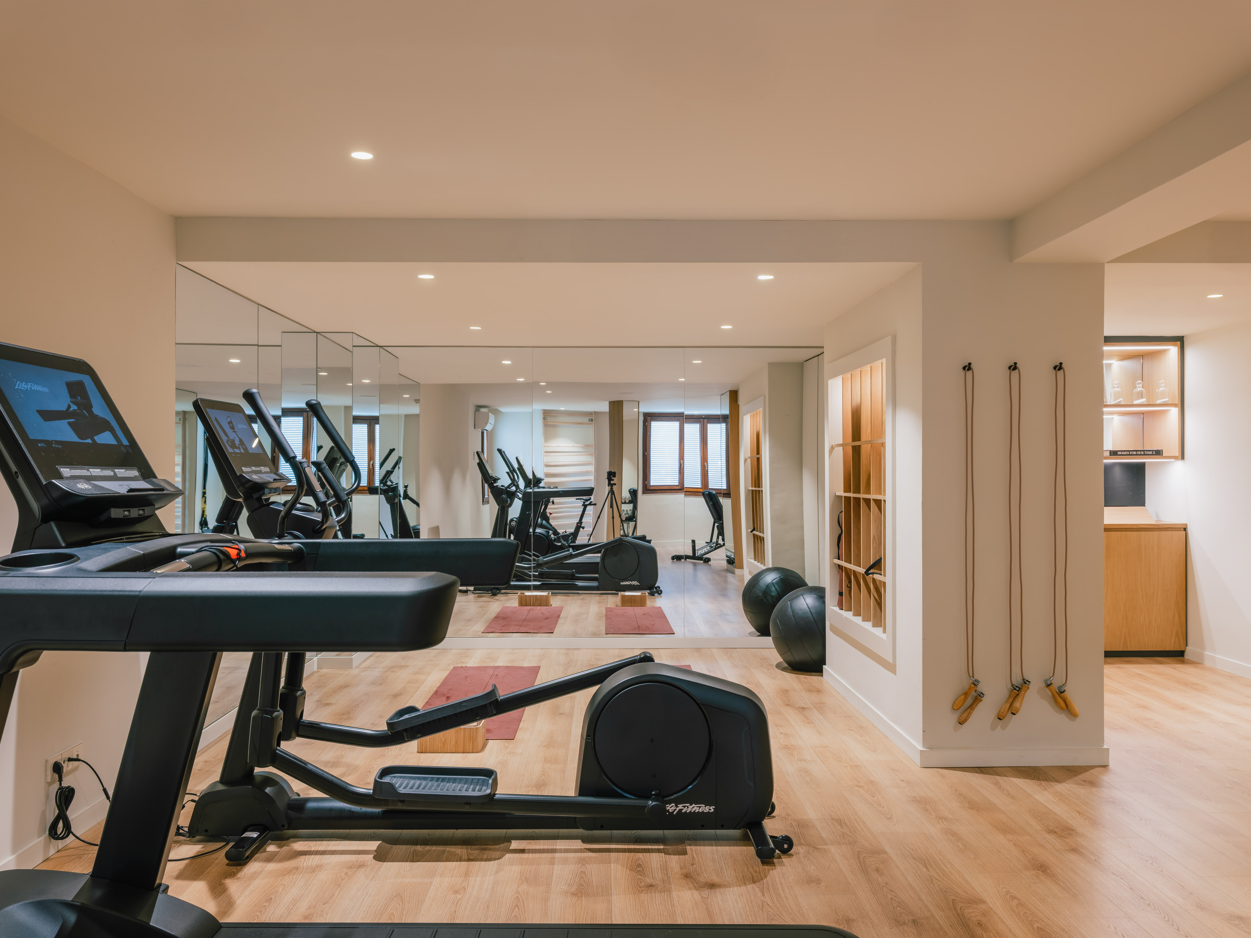 Modern home fitness gym with treadmill, elliptical, and mirrors on wooden floor.