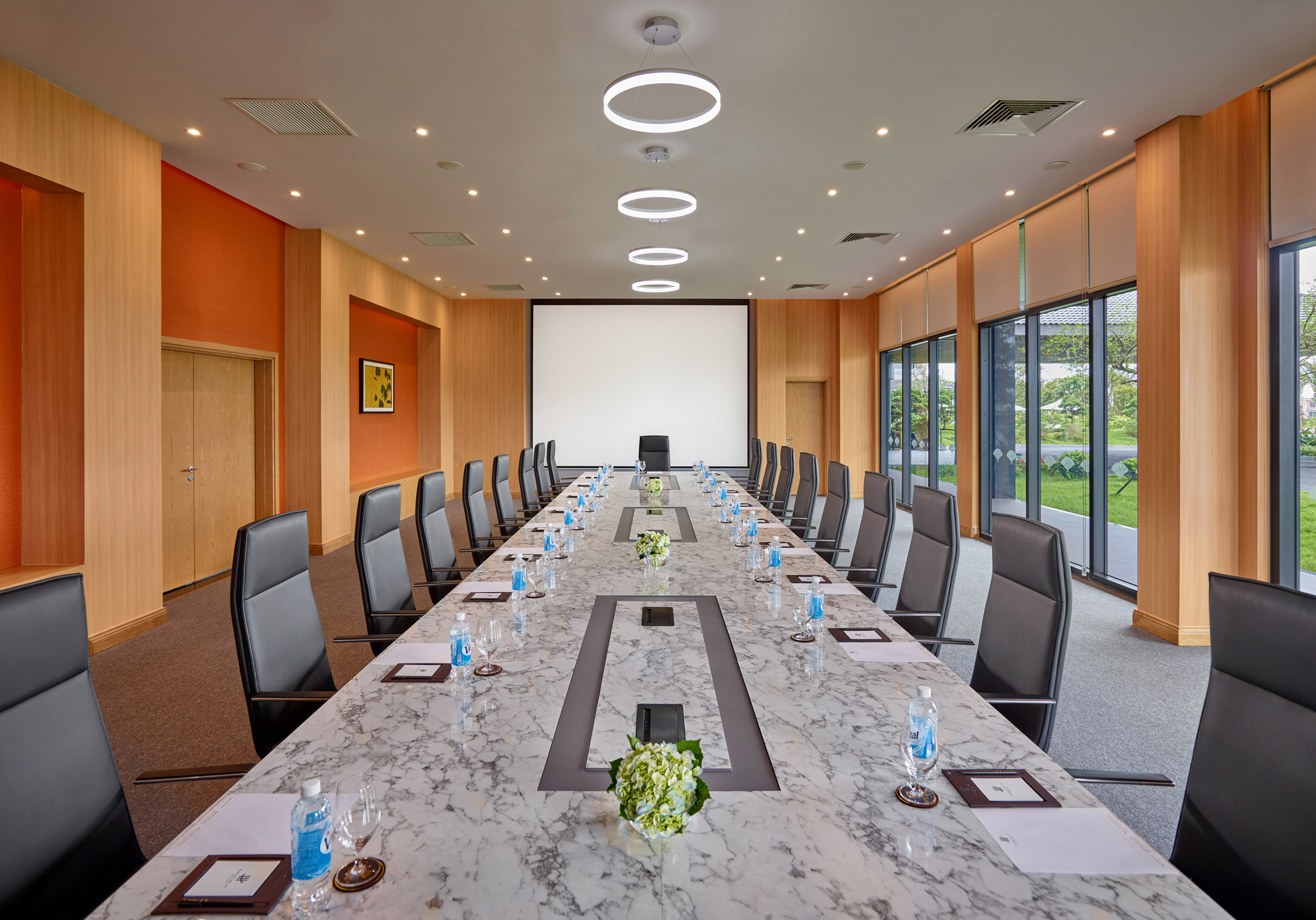 Modern boardroom with long marble table, black chairs, and projection screen.