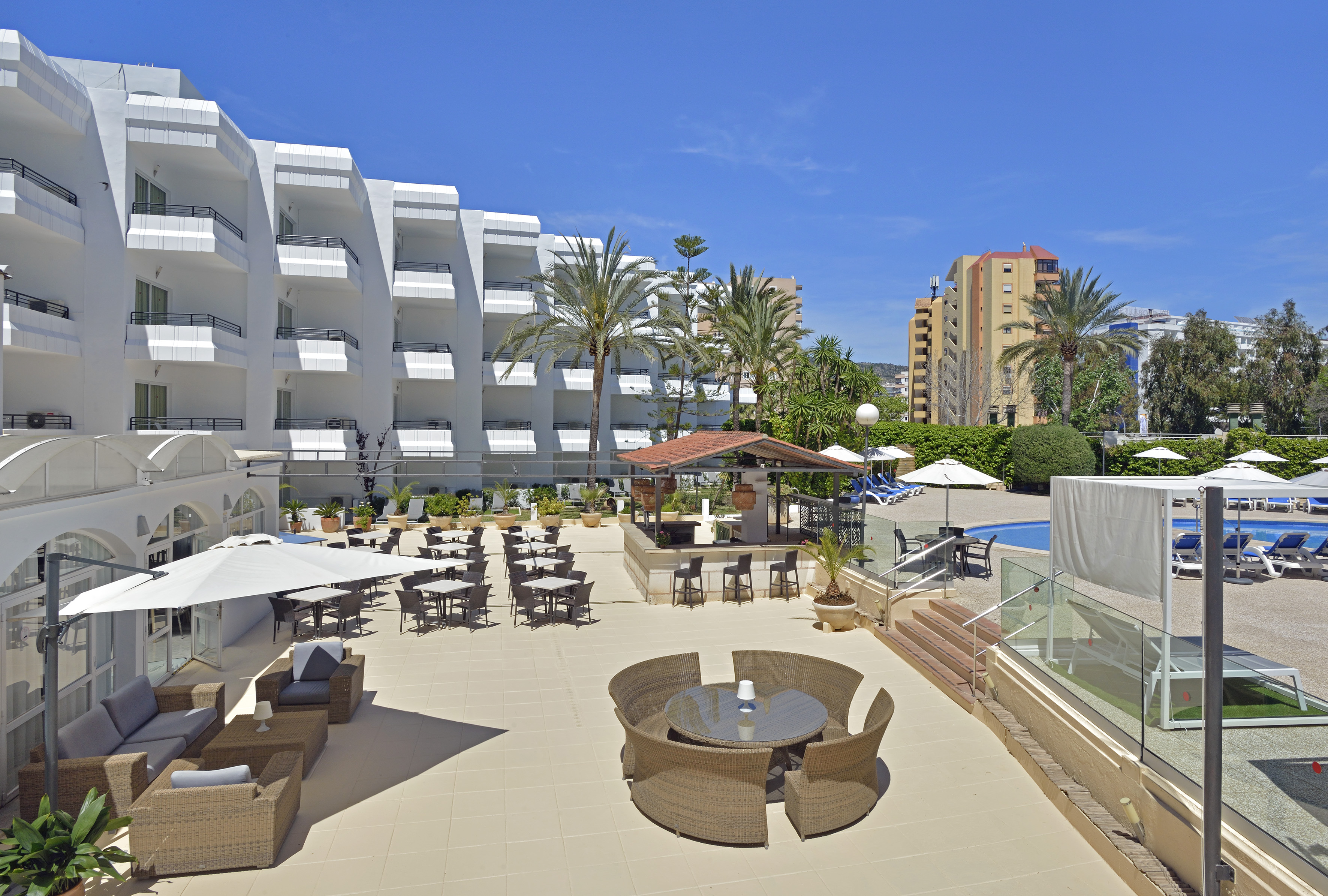 Hotel resort outdoor terrace with pool, bar, lounge, and palm trees.