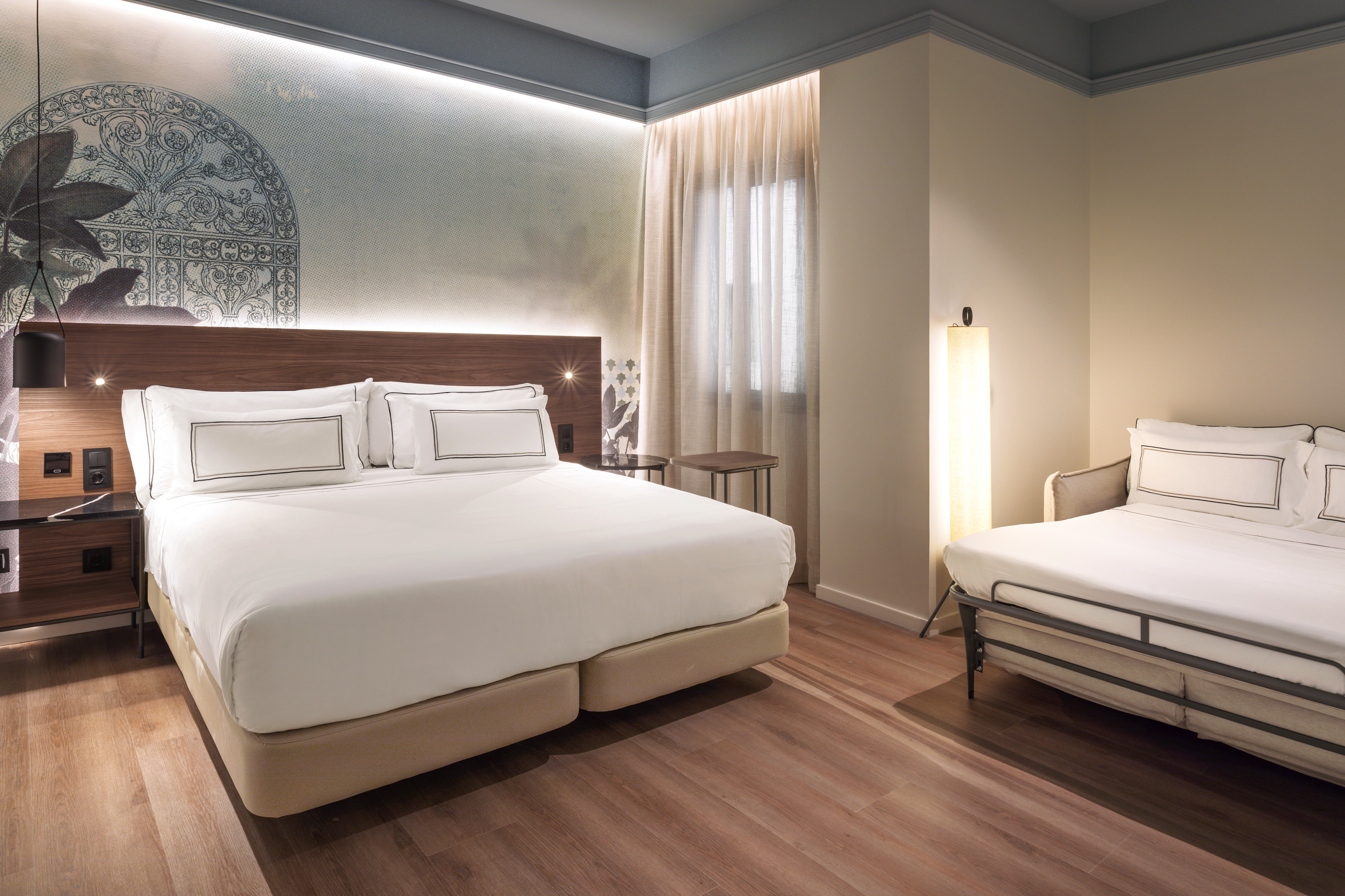Modern hotel room with king bed, sofa bed, wood floor, and accent wall.