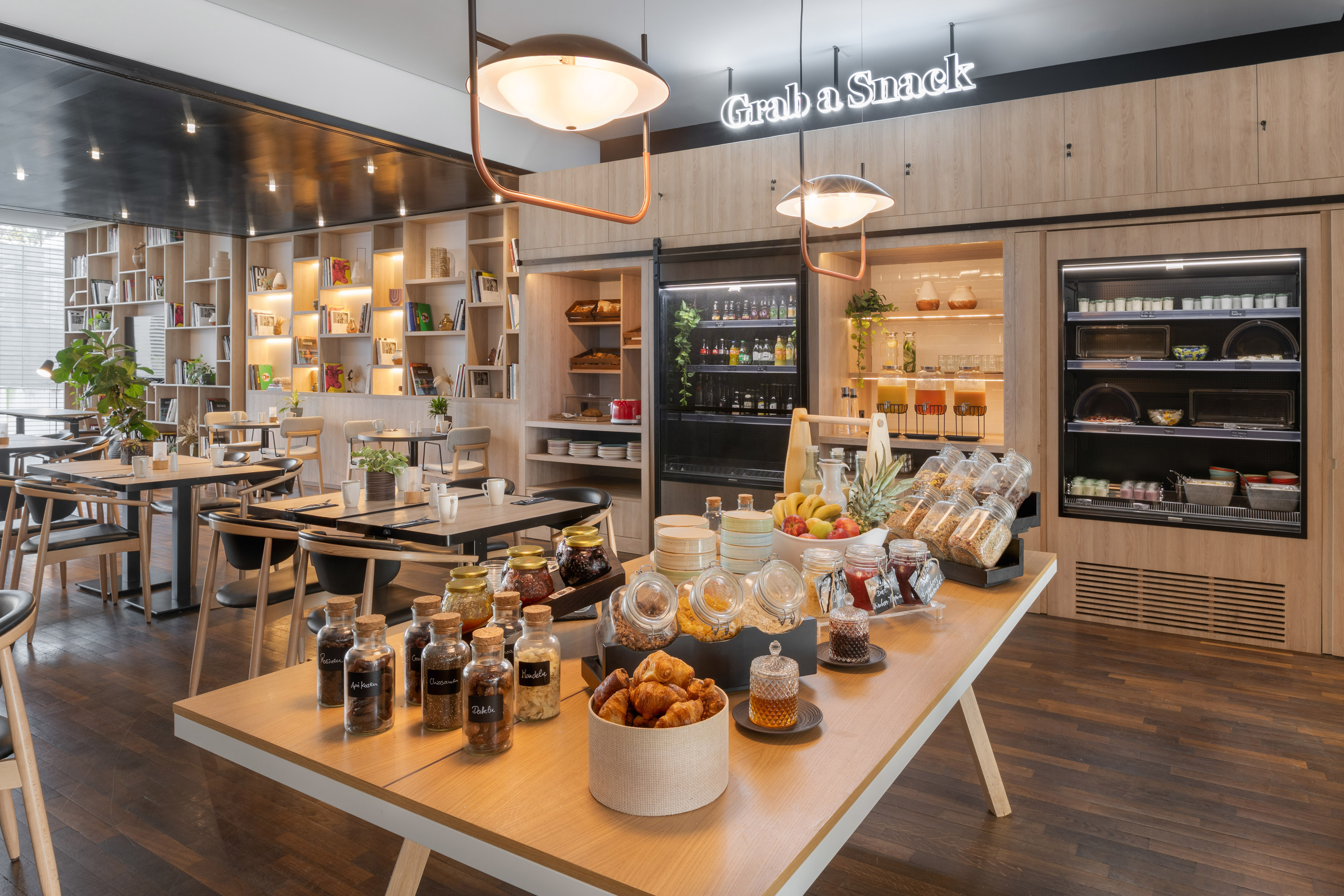 Modern hotel breakfast buffet with pastries, fruits, and a "Grab a Snack" sign.