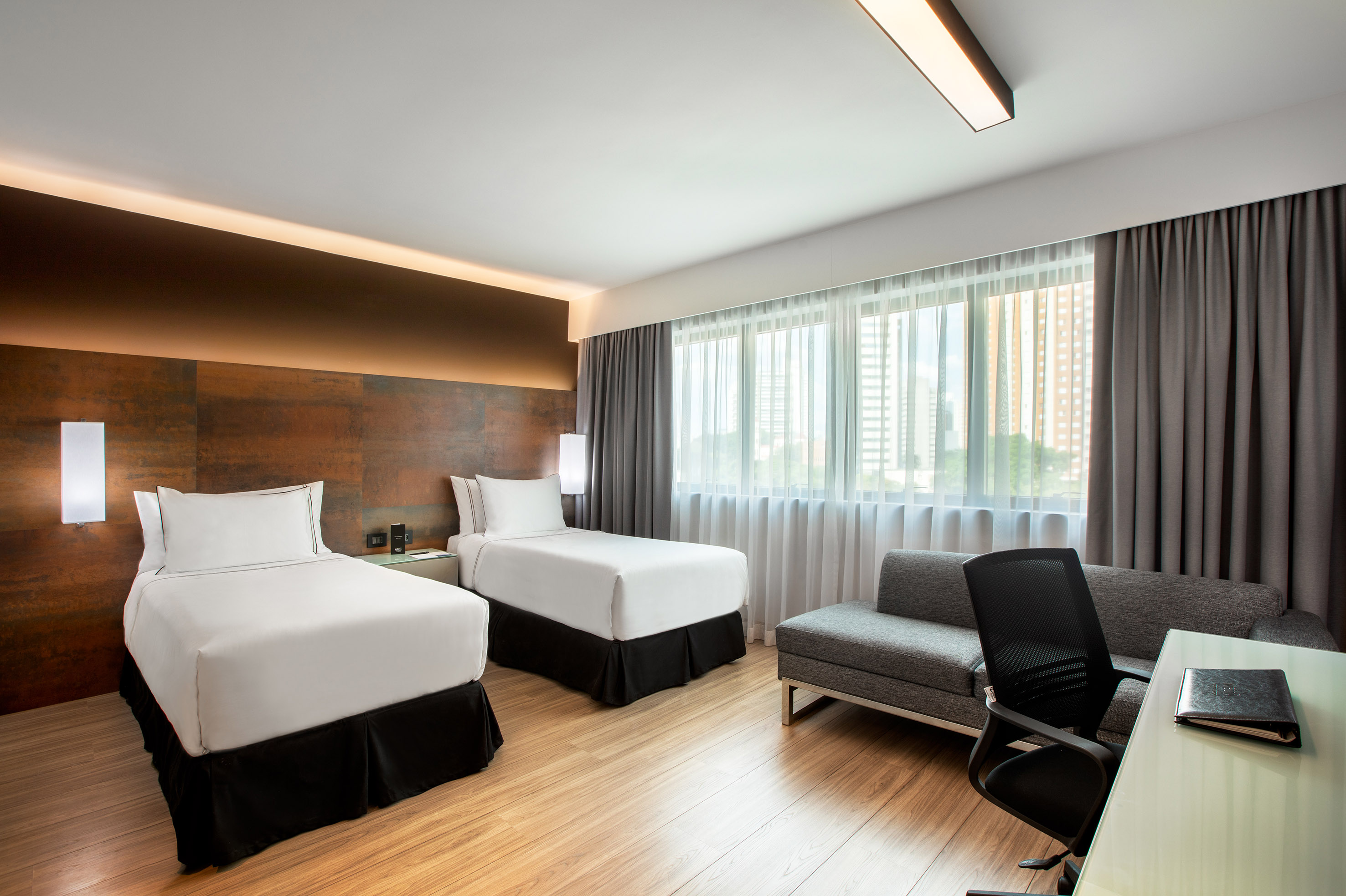 Modern hotel room with two twin beds, work desk, and seating area by window.