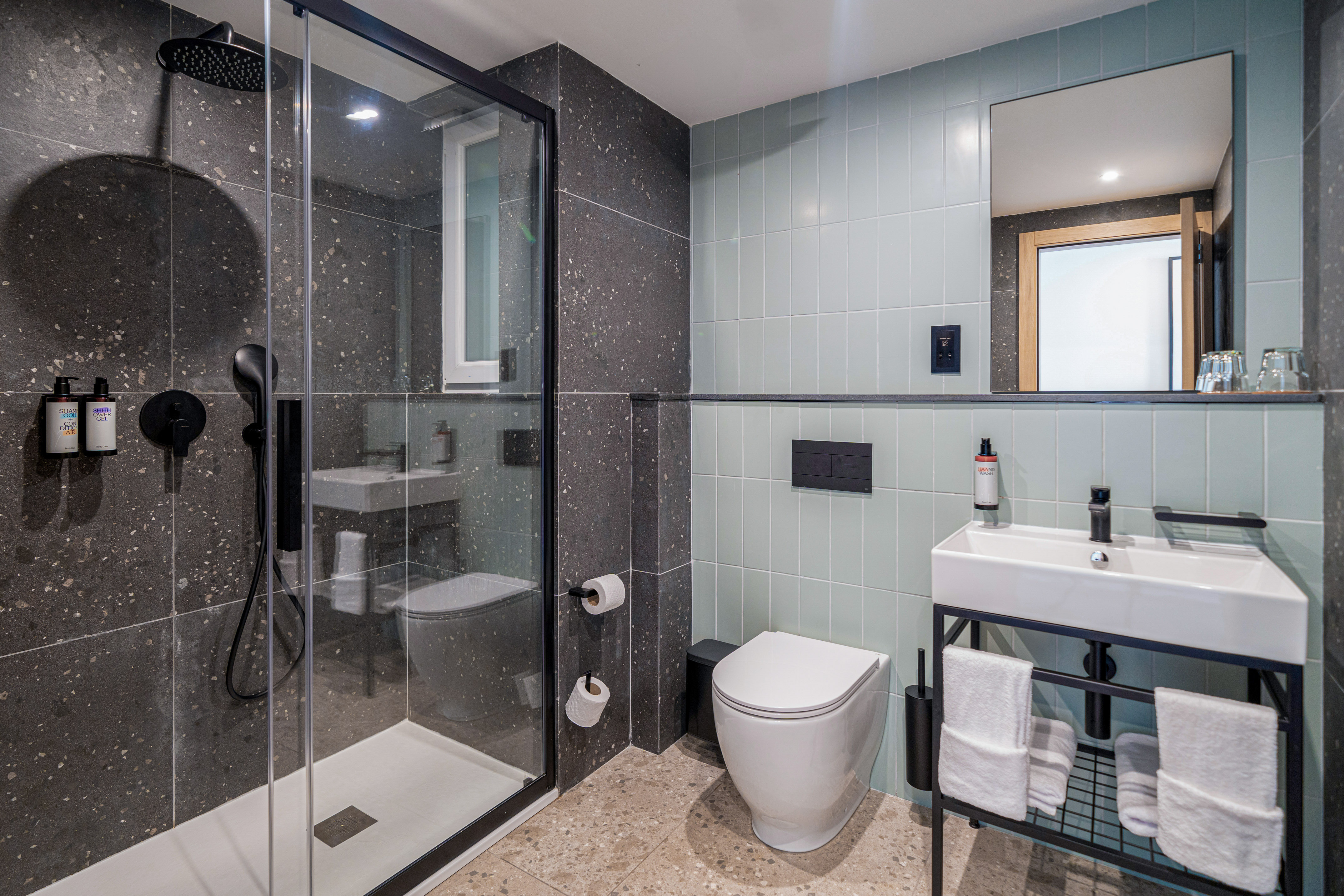 Modern bathroom with glass shower, toilet, sink, grey & blue tiles, black fixtures.