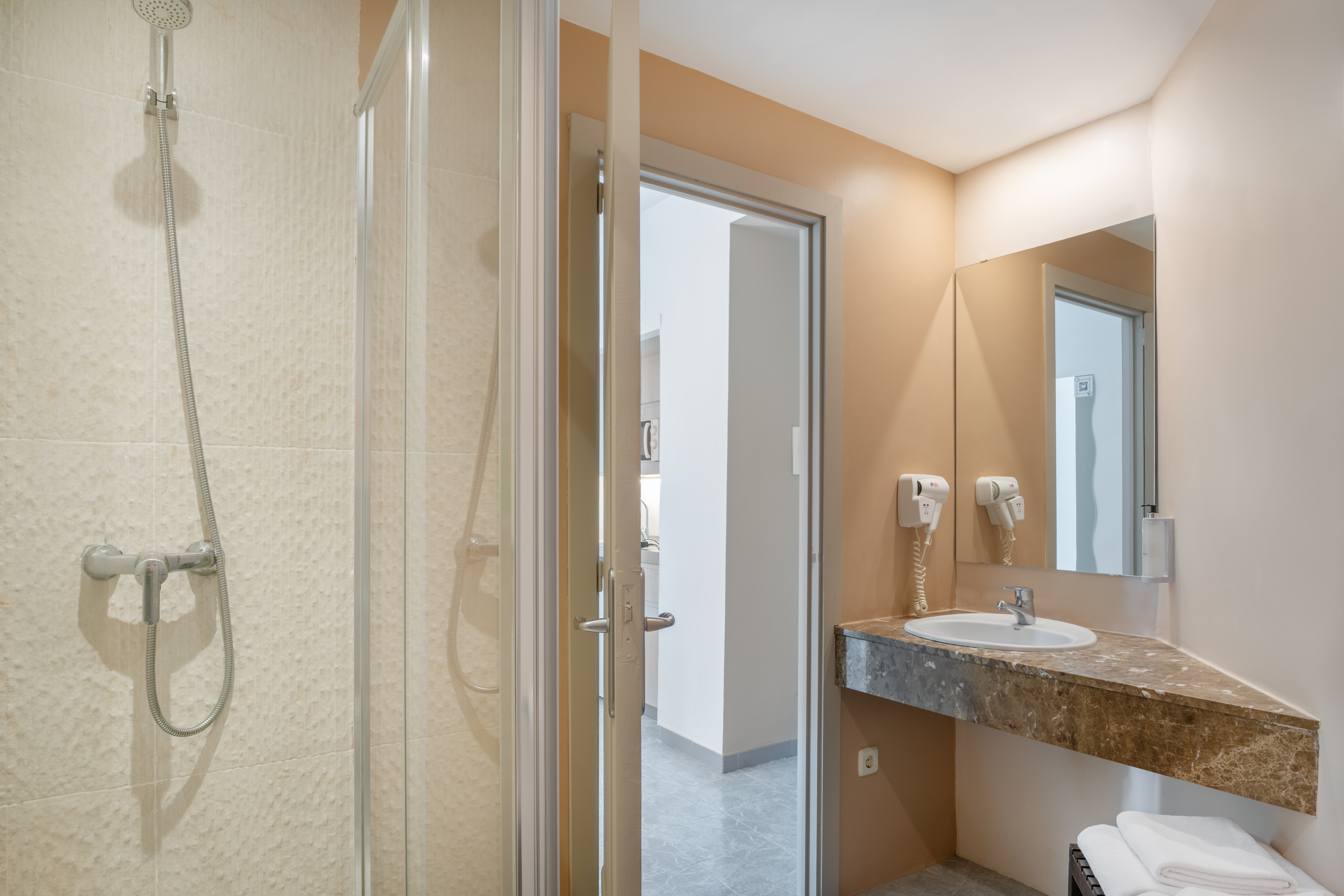 Hotel bathroom with walk-in shower, marble vanity, sink, mirror, towels.