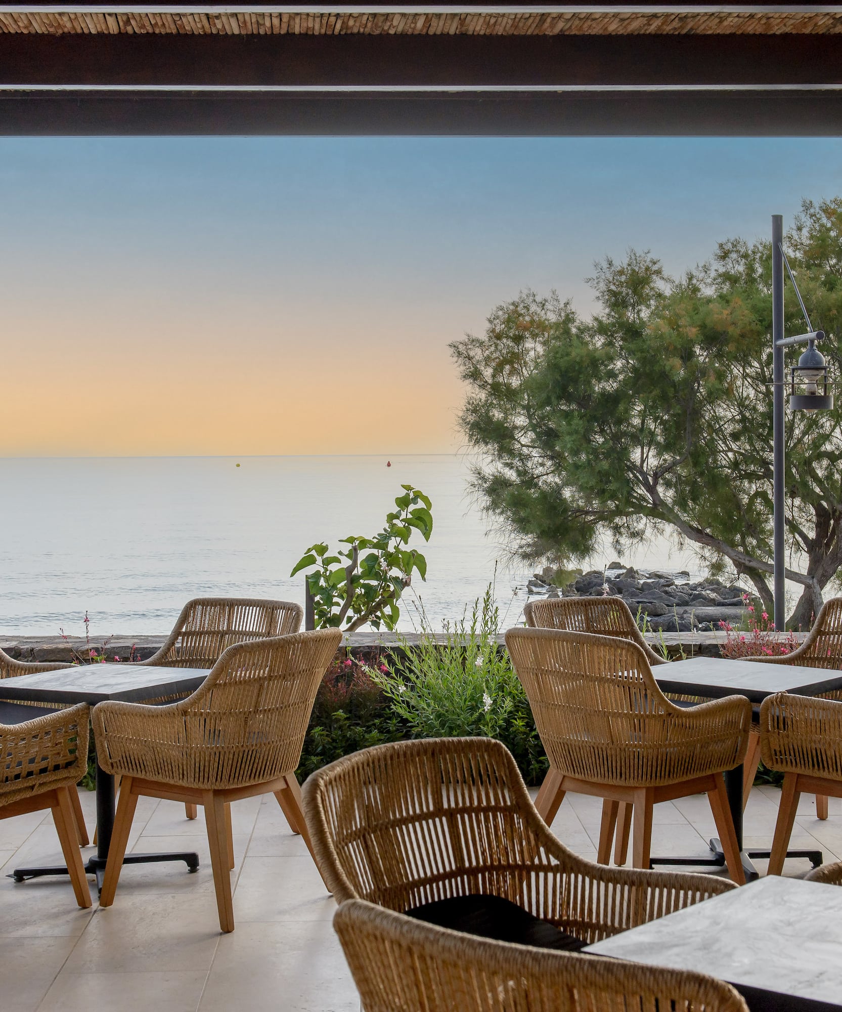 Coastal dining patio with wicker chairs, tables, and ocean sunset view.