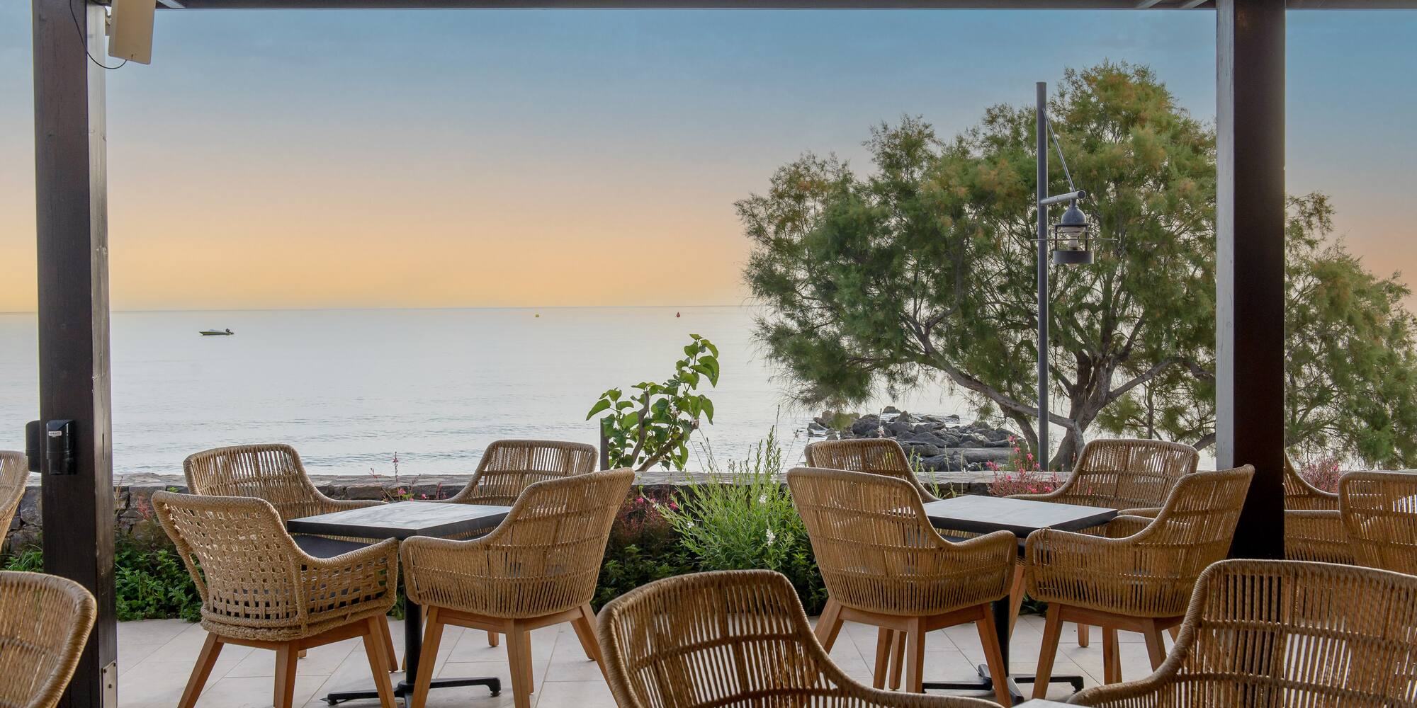 Waterfront dining patio with wicker chairs, ocean view at sunset.