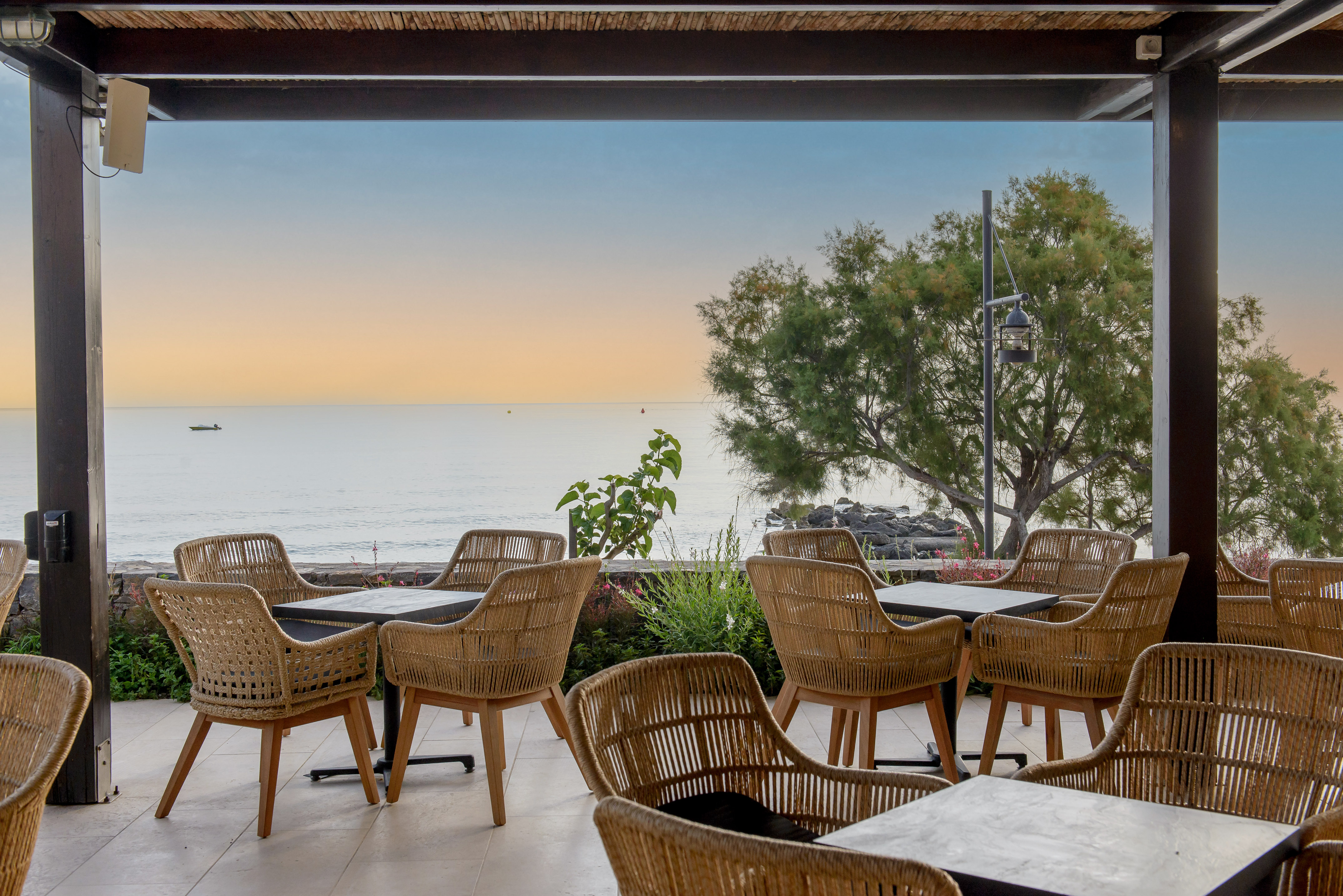 Coastal dining patio with wicker chairs, tables, and ocean sunset view.