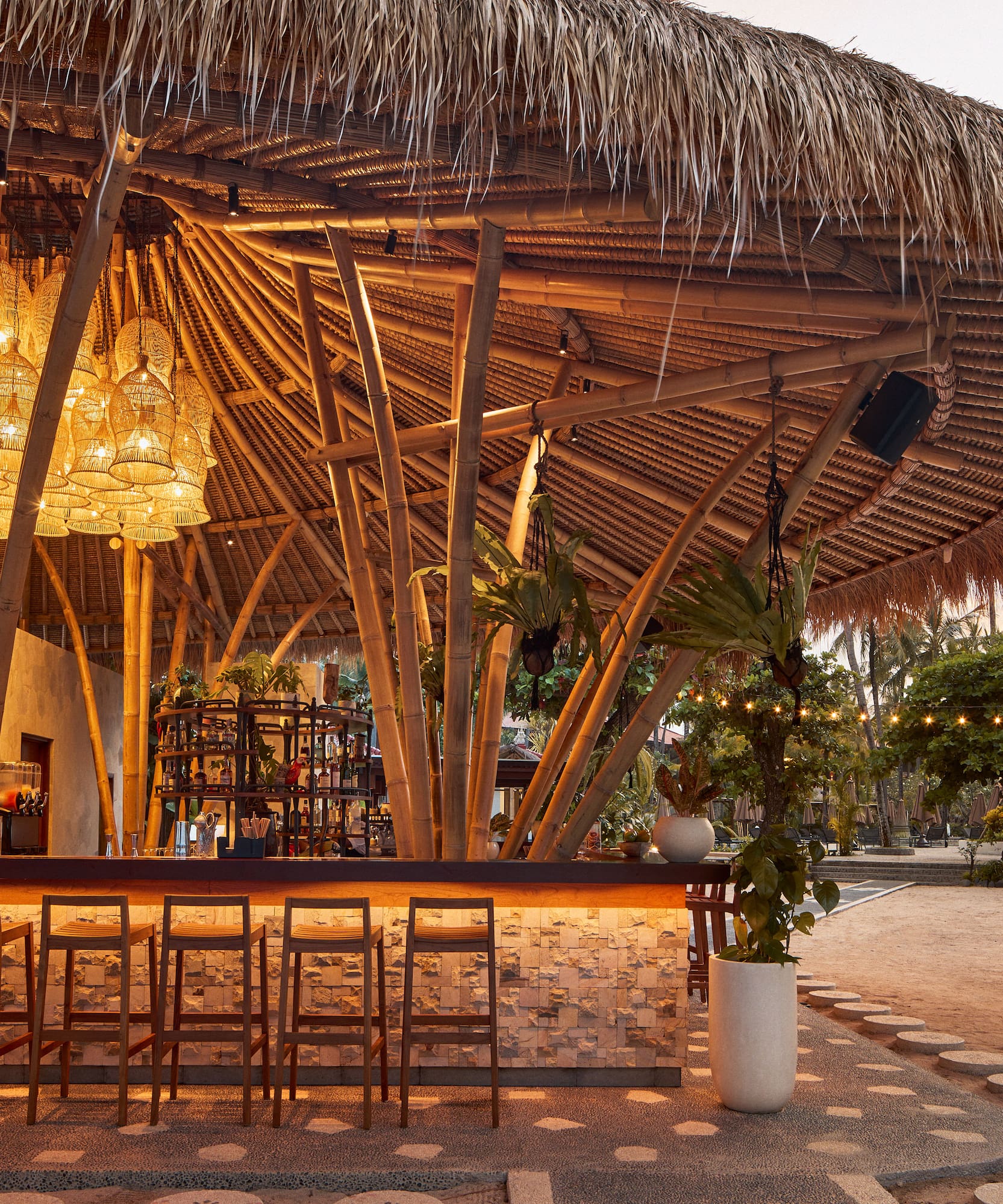 Tropical resort bar with bamboo structure, thatched roof, and warm lighting.