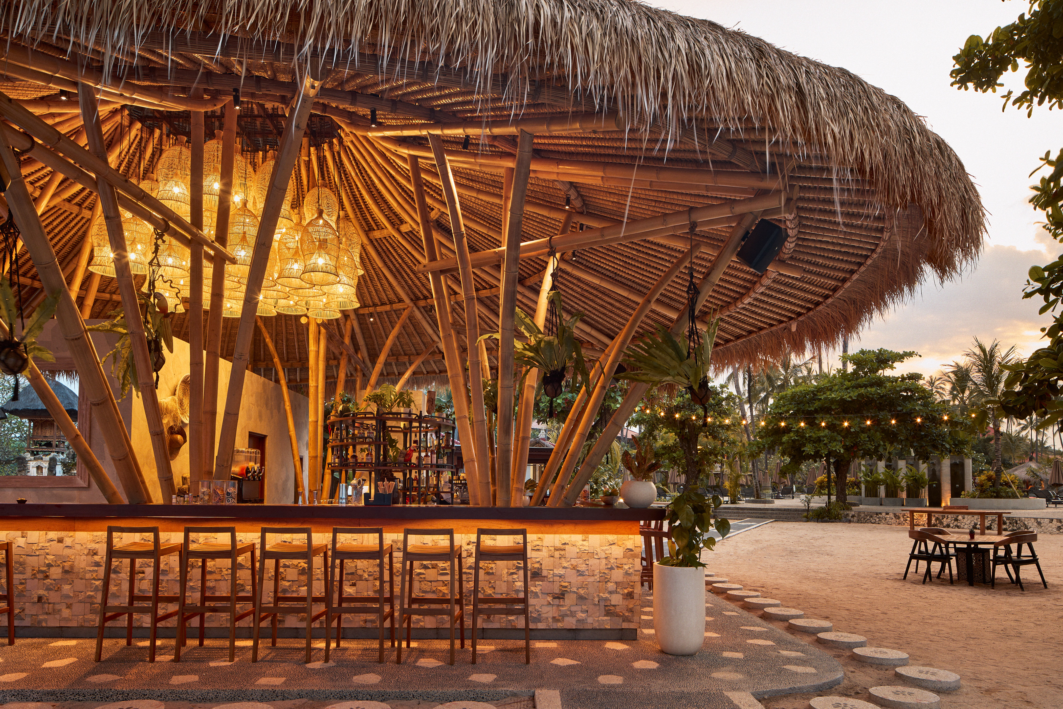 Tropical resort bar with bamboo structure, thatched roof, and warm lighting.