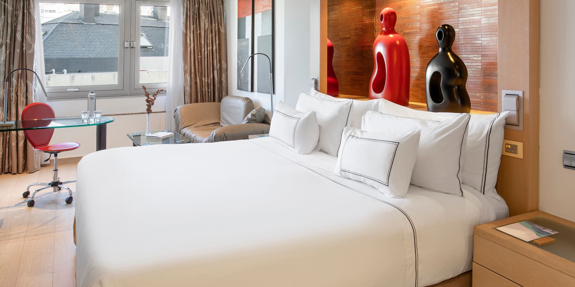 a bed with white sheets and pillows in a room with a red and black sculpture
