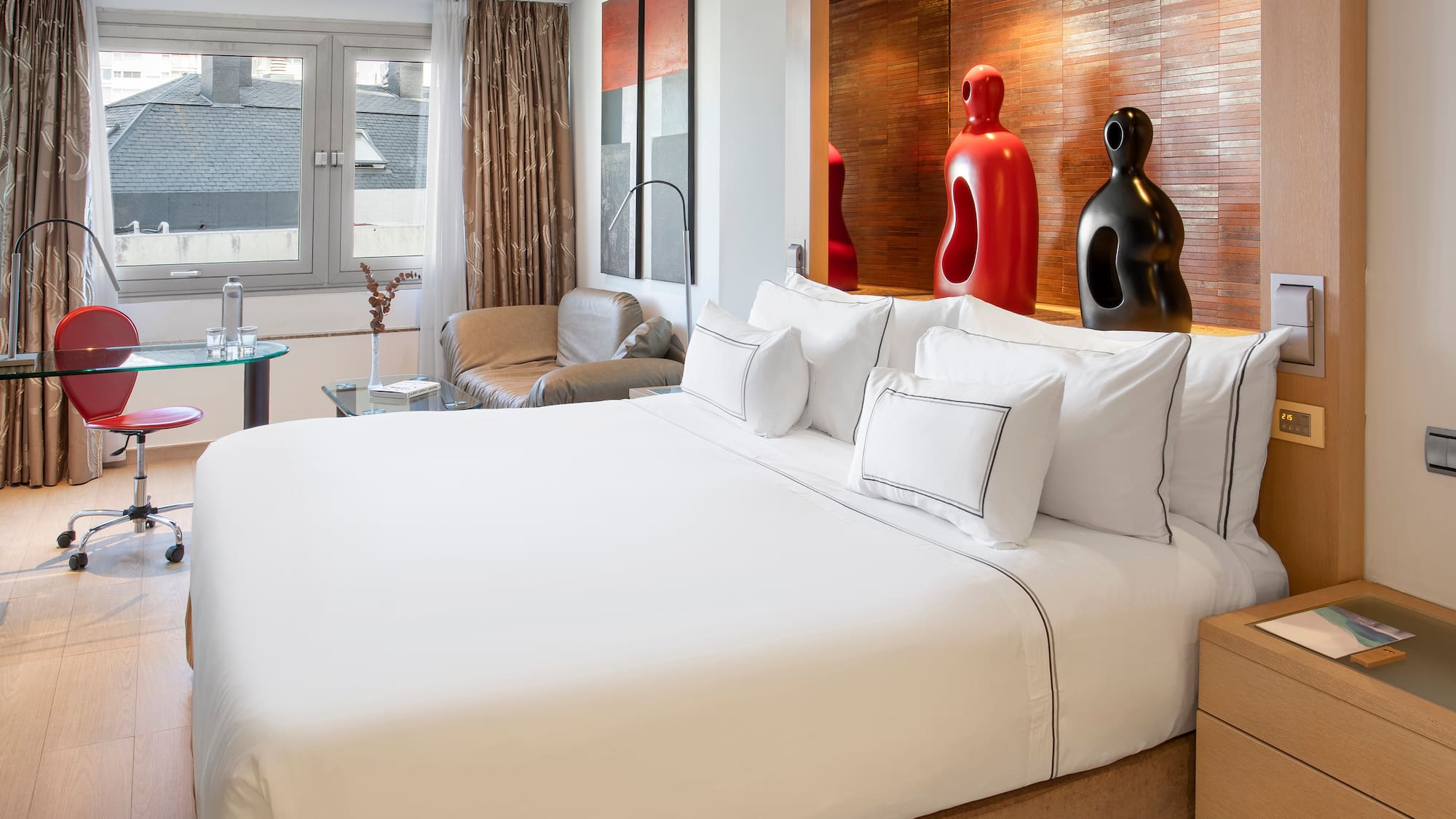 a bed with white sheets and pillows in a room with a red and black sculpture