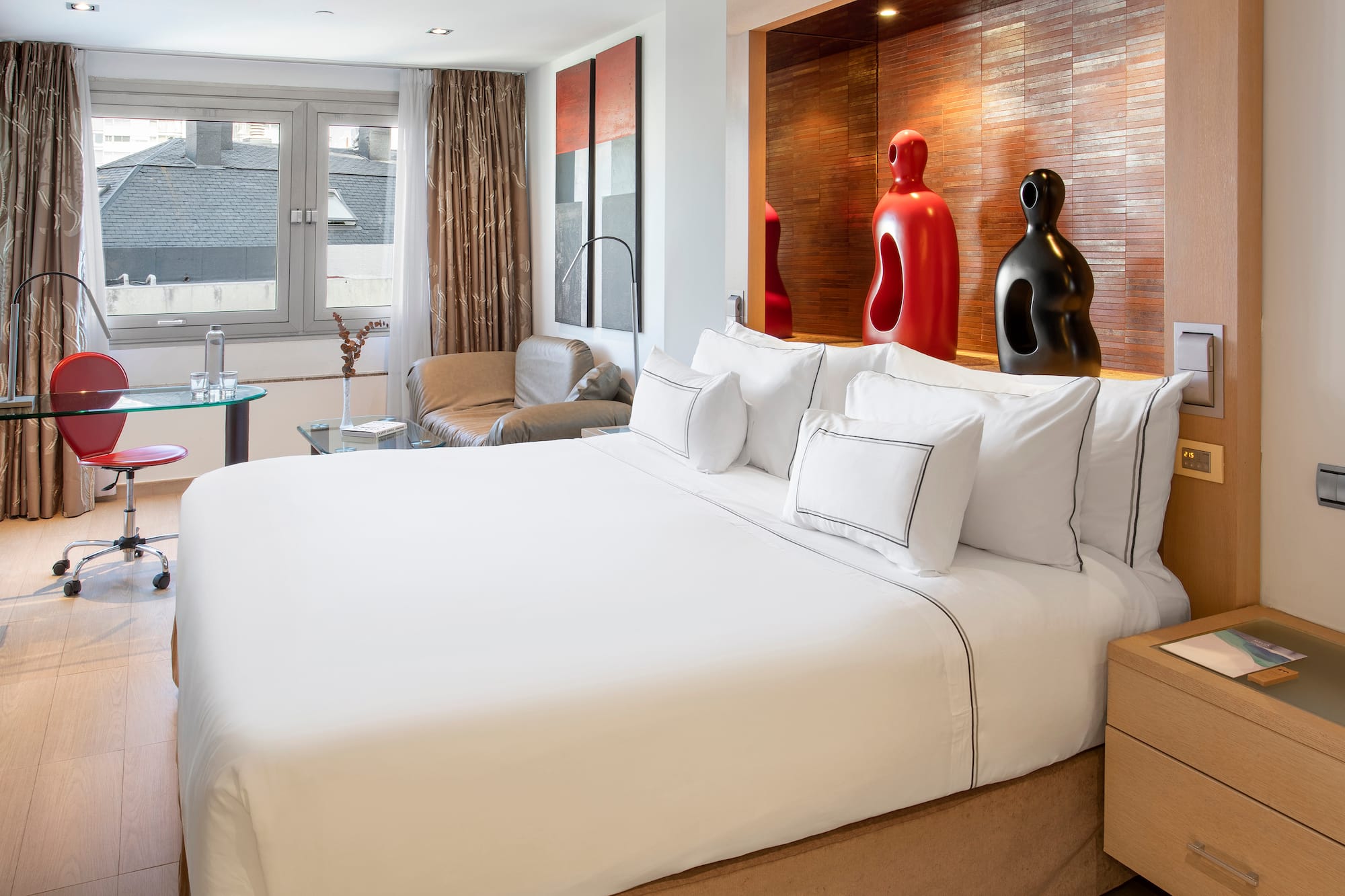 a bed with white sheets and pillows in a room with a red and black sculpture