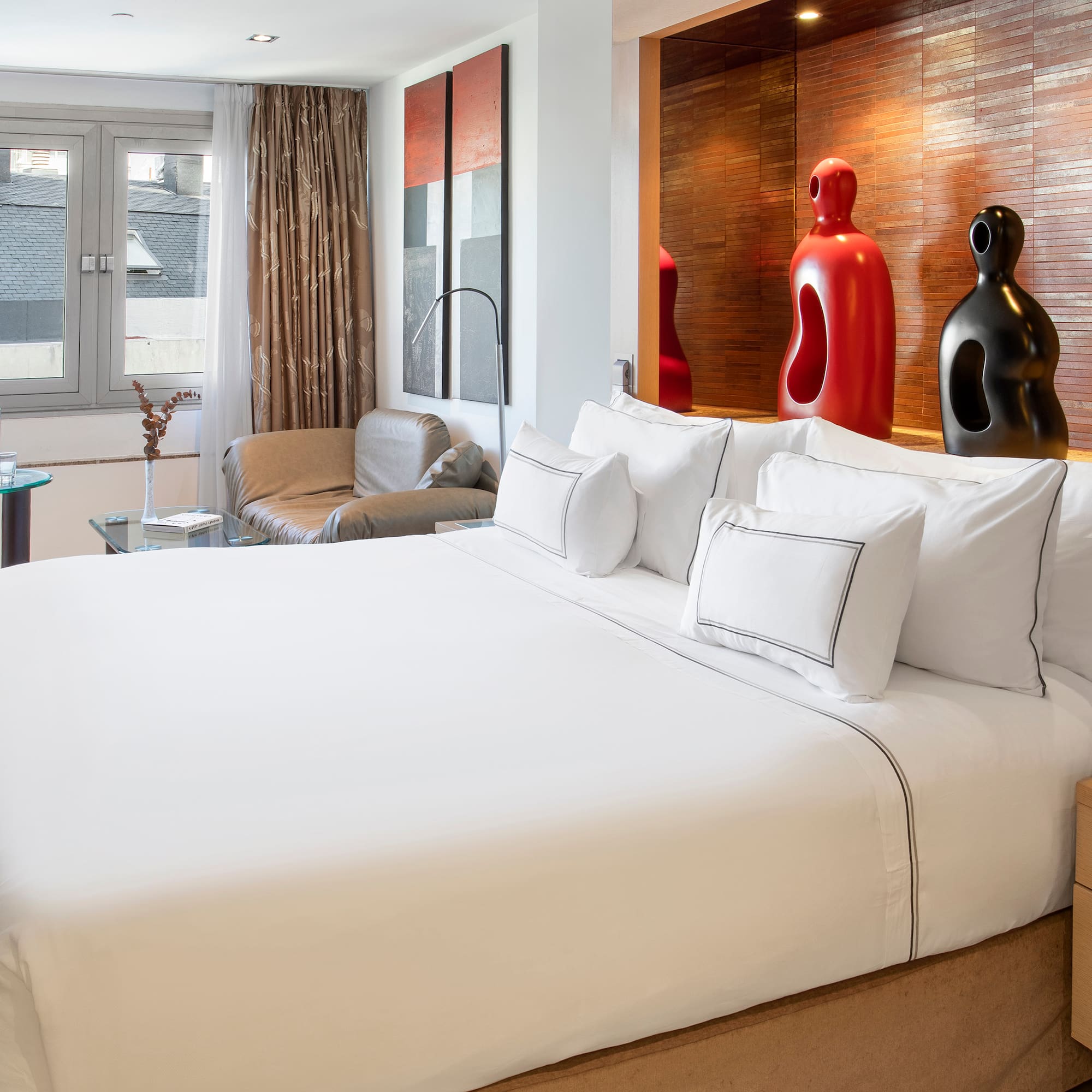 a bed with white sheets and pillows in a room with a red and black sculpture