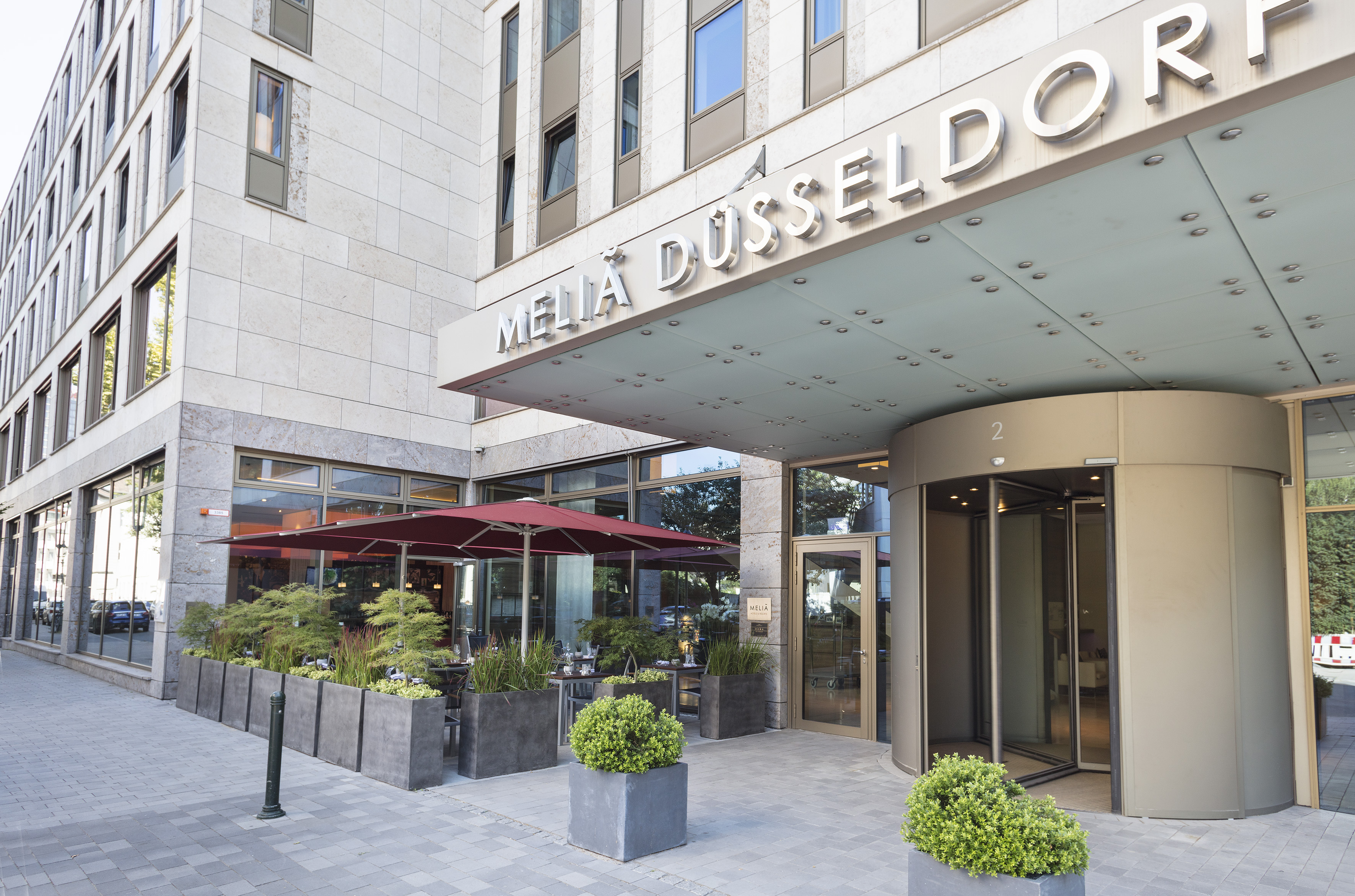 Meliá Düsseldorf hotel exterior, sign, revolving door, outdoor cafe seating, planters.