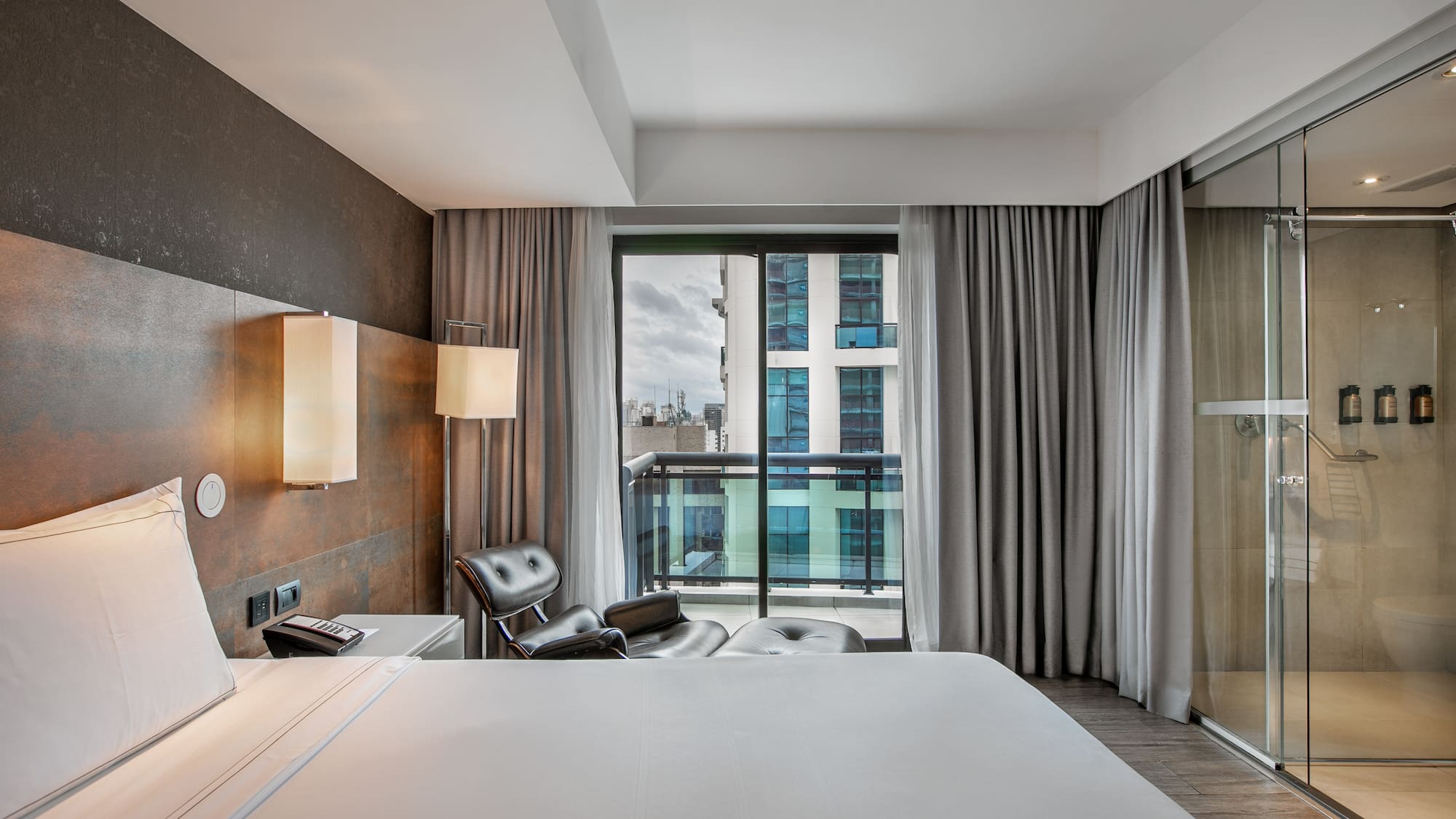 Quarto de hotel moderno com cama grande, poltrona, varanda e banheiro de vidro. - Grand Premium com Varanda - Meliá Ibirapuera, São Paulo