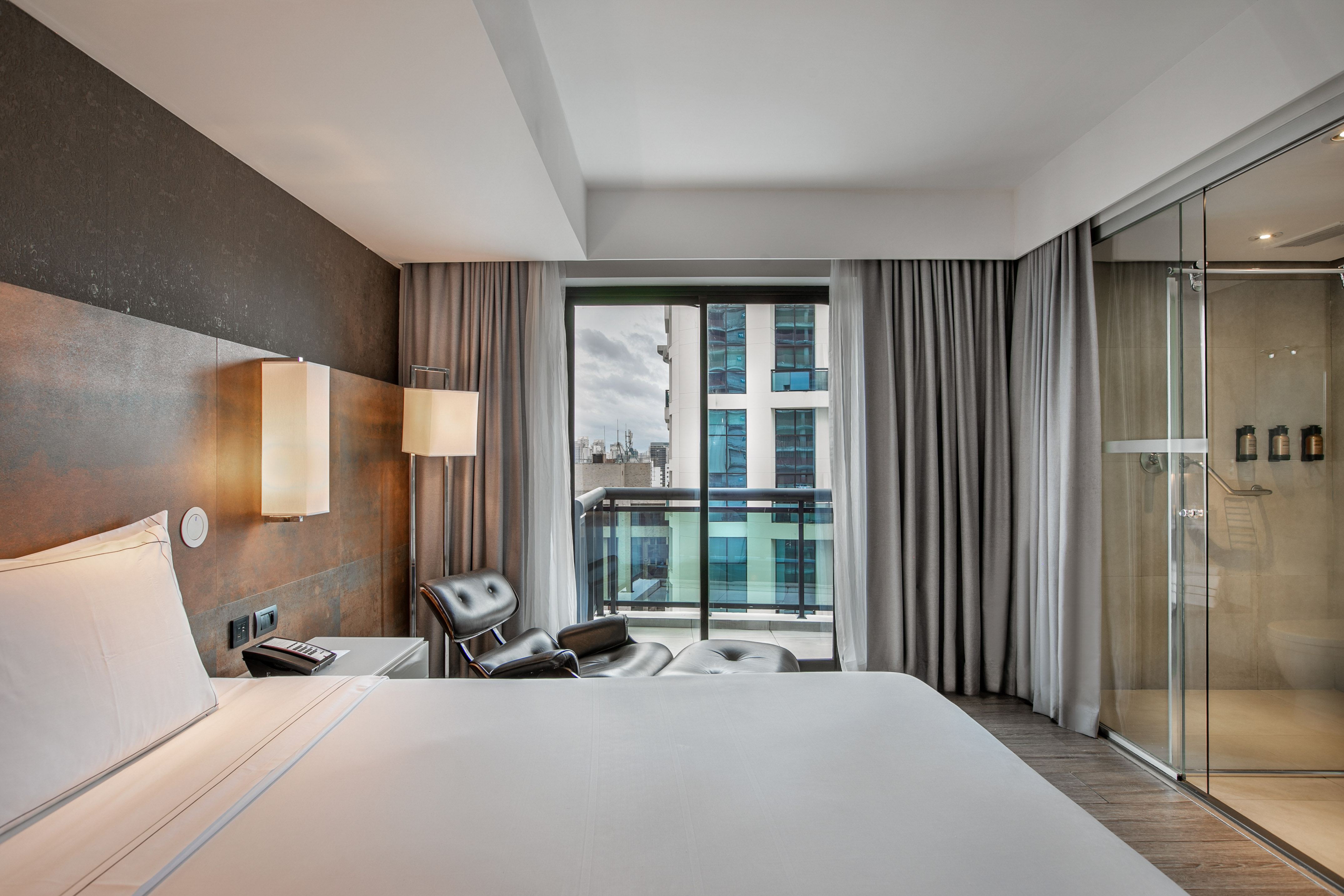 Quarto de hotel moderno com cama grande, poltrona, varanda e banheiro de vidro. - Grand Premium com Varanda - Meliá Ibirapuera, São Paulo