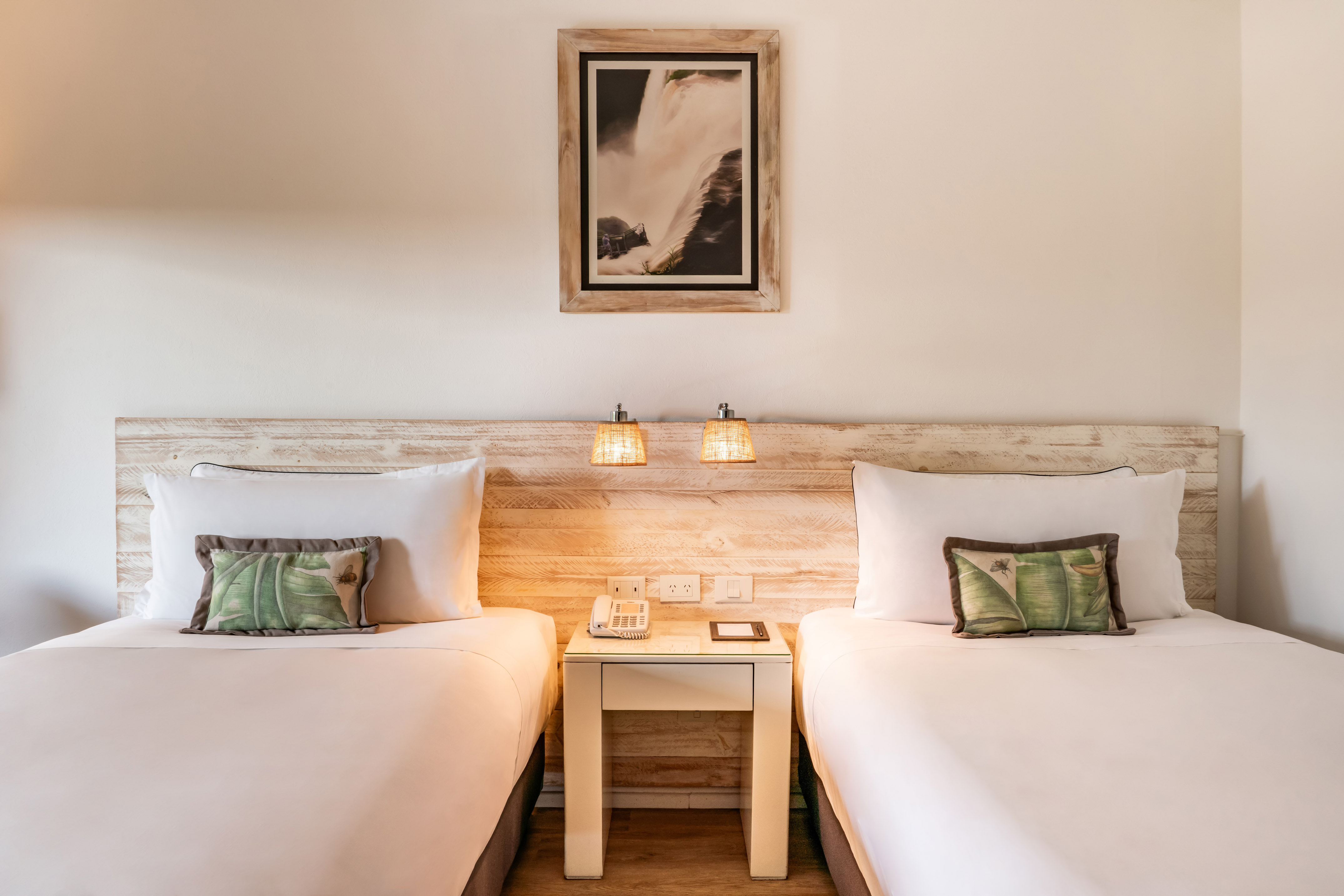 Bright hotel room with two twin beds, rustic wood headboard, and bedside lamps.