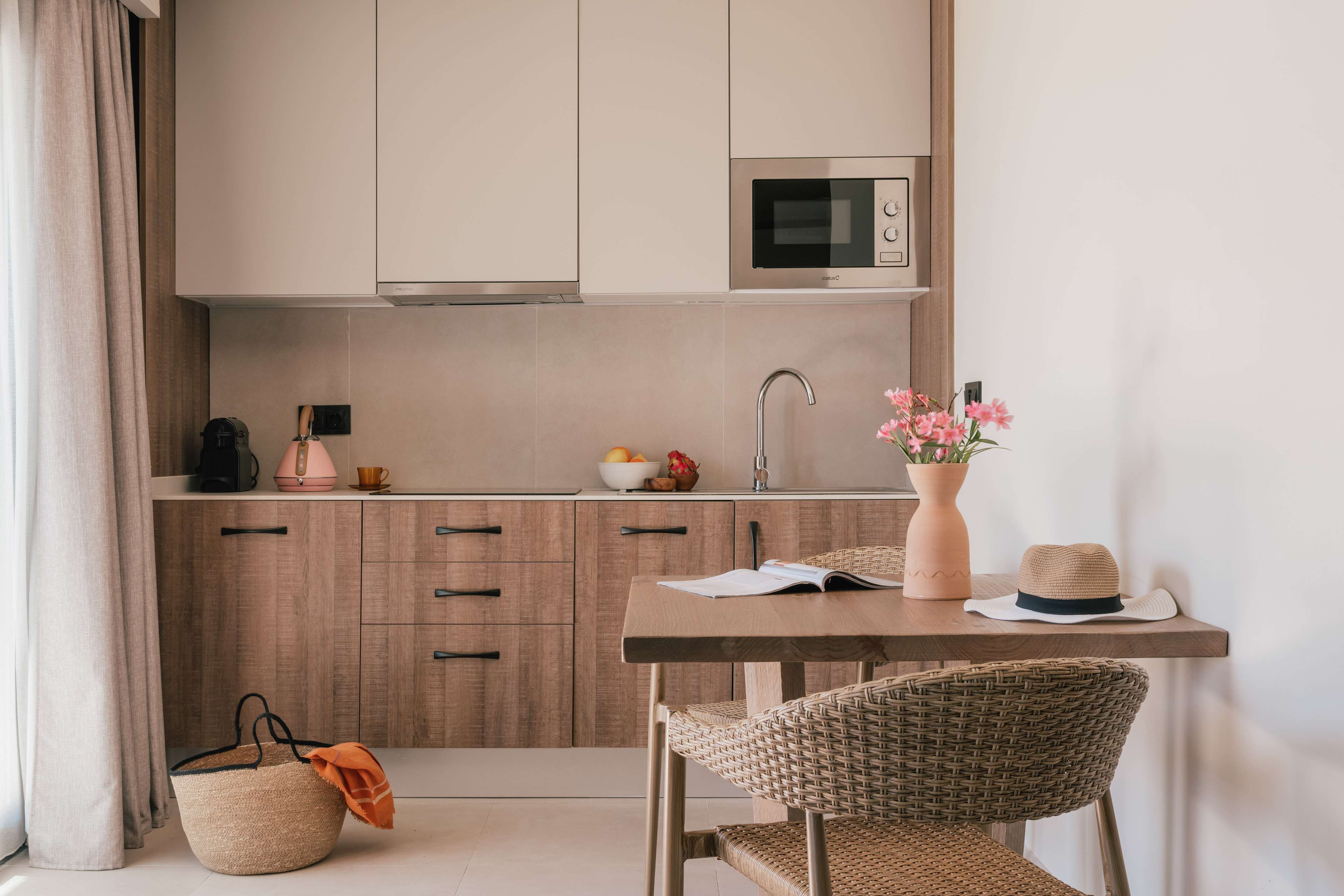 Modern kitchen/dining area: wood cabinets, built-in microwave, wicker chairs, flowers.
