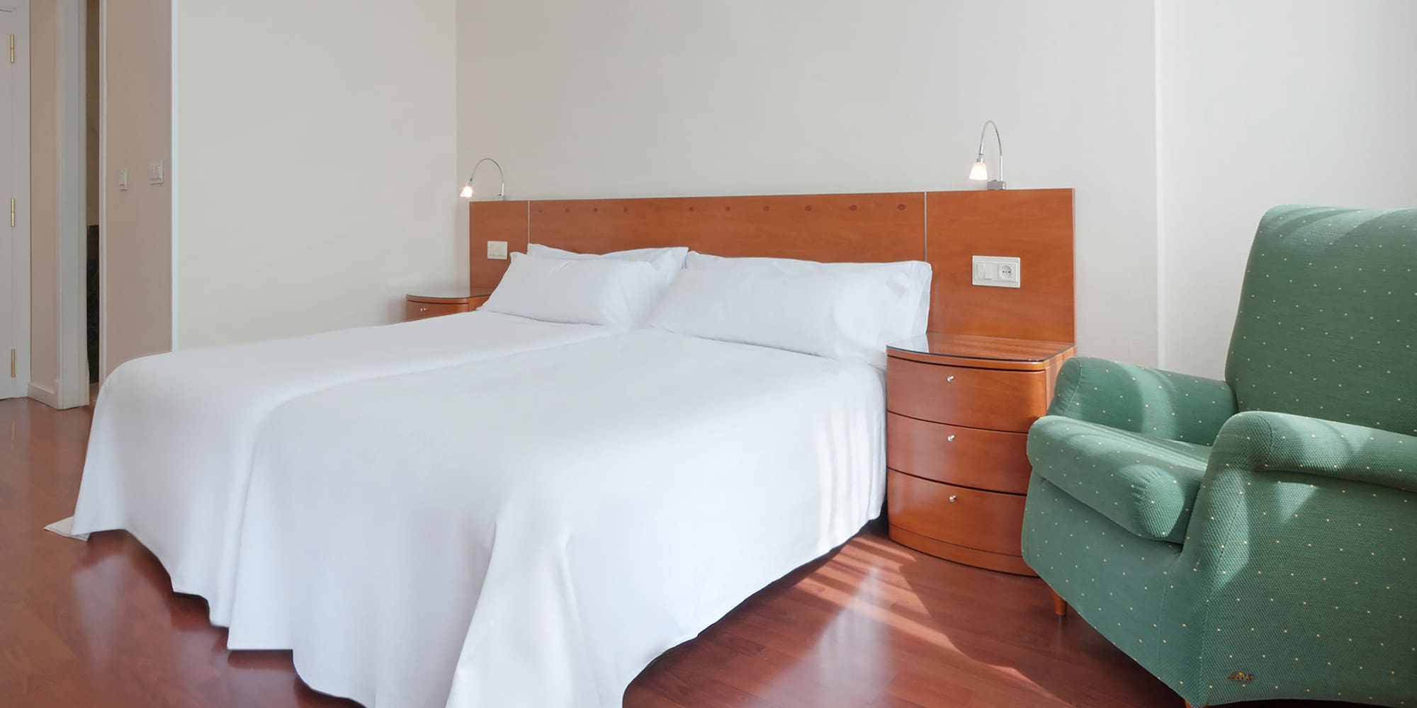 a bed with white sheets and a green chair