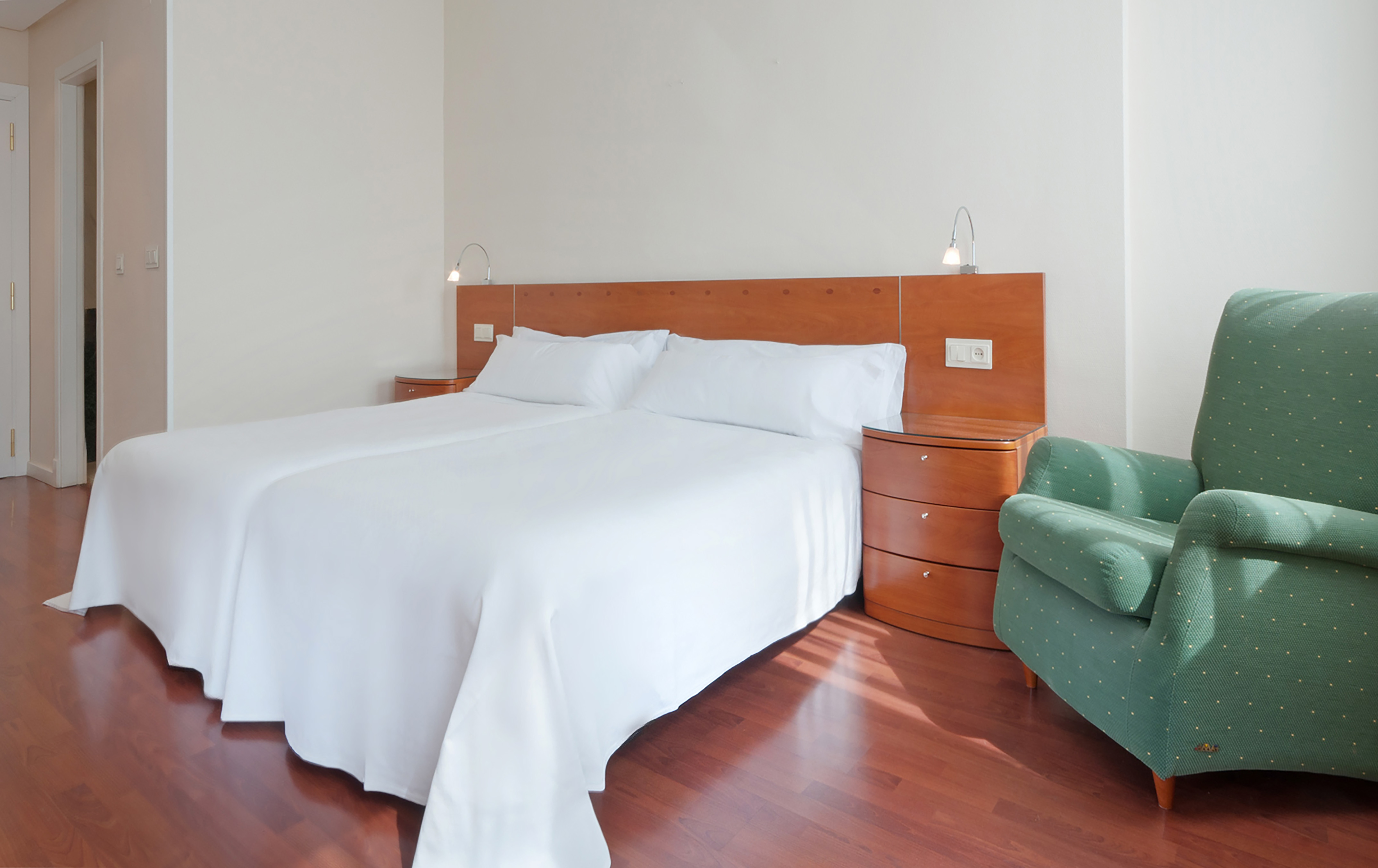 Hotel room with twin beds, white bedding, wood nightstands, and green chair.