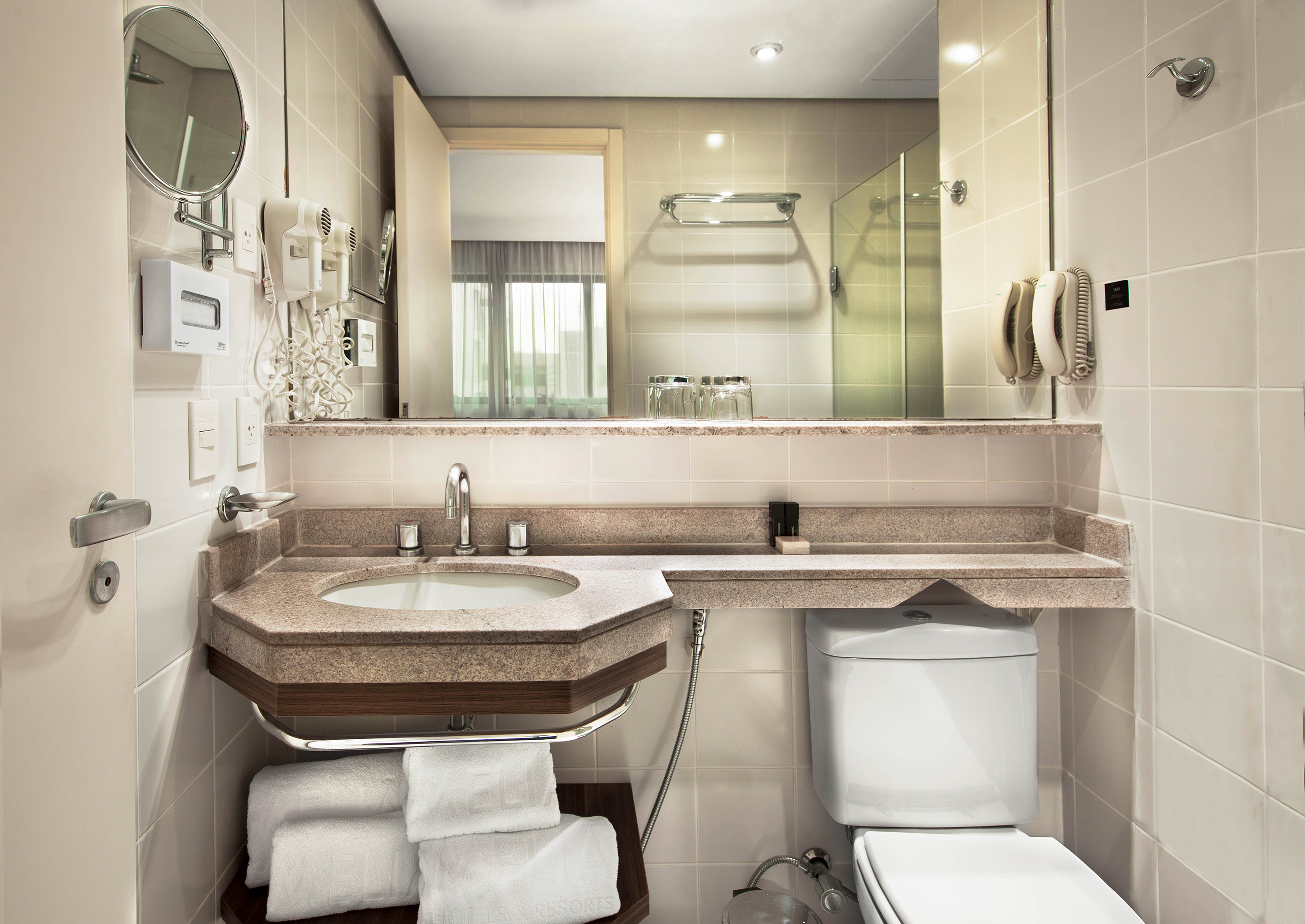 Modern hotel bathroom with vanity, sink, large mirror, toilet, and folded towels.