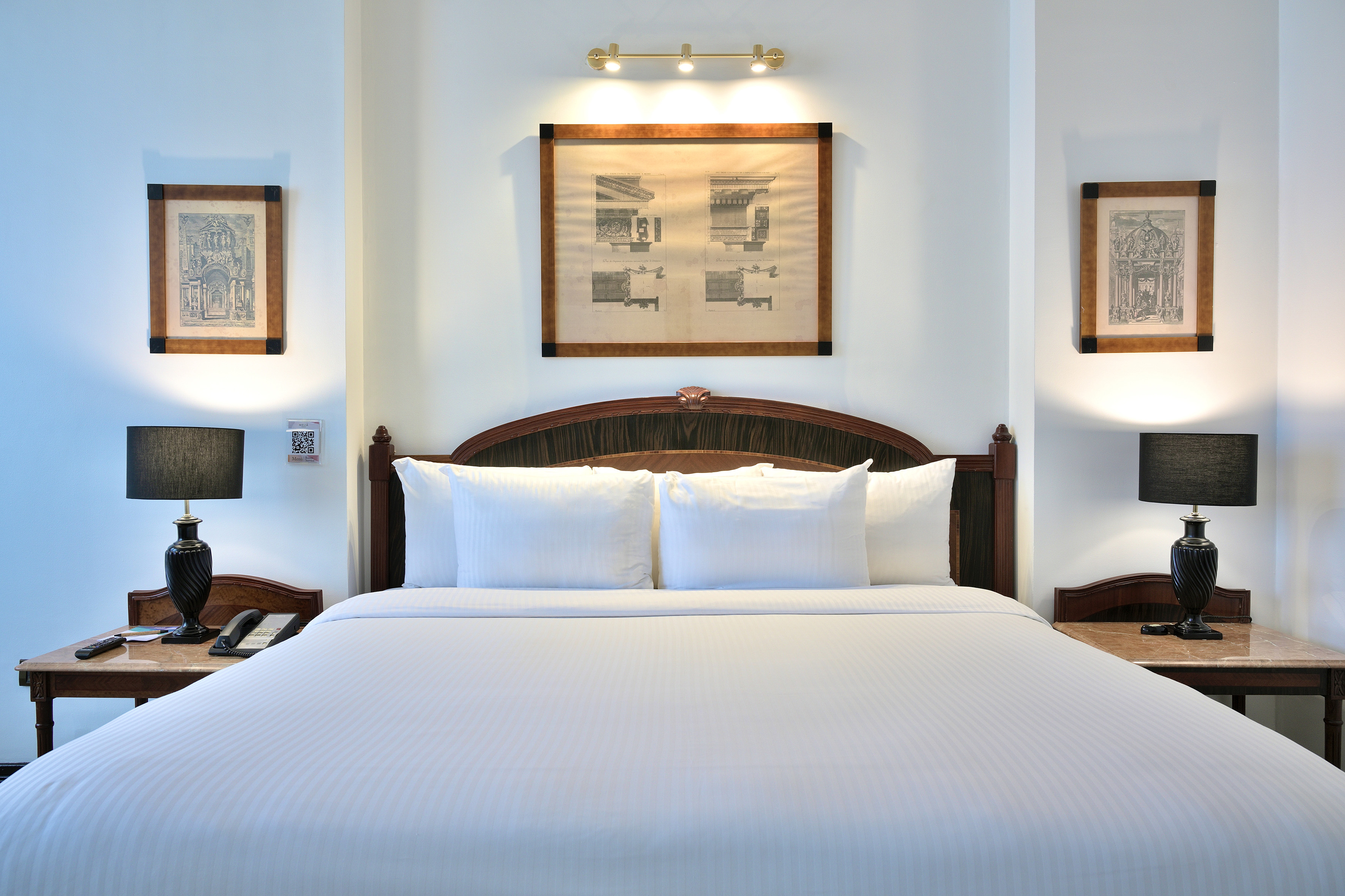 Hotel room with king bed, white bedding, dark wood headboard, and bedside lamps.