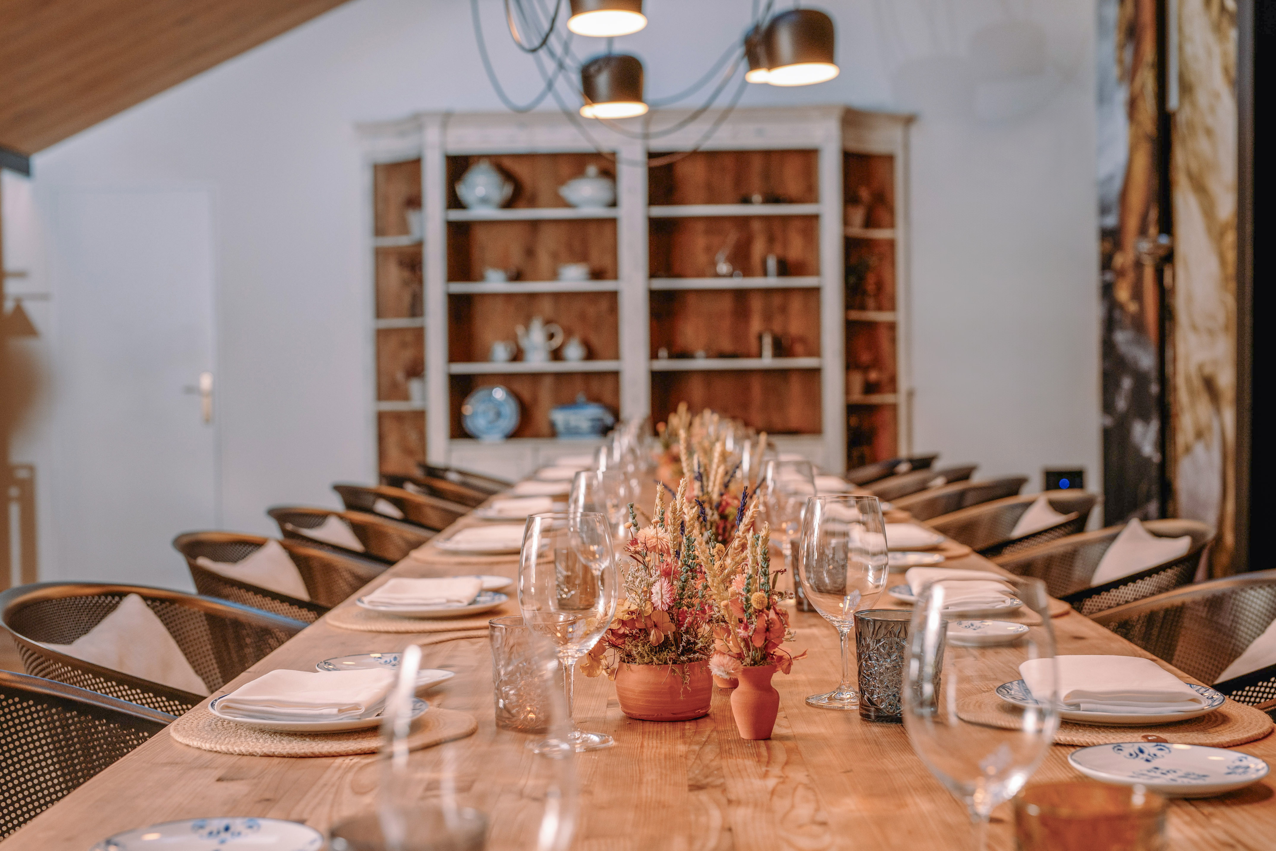 Set long wooden dining table with floral centerpieces for an event.