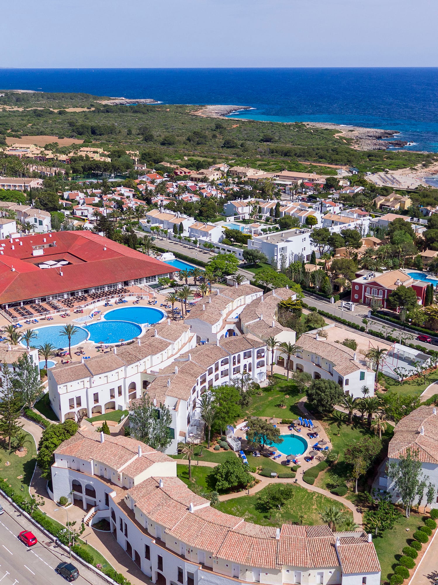 Aerial view: Mediterranean coastal resort with pools, hotel, and sandy beach.