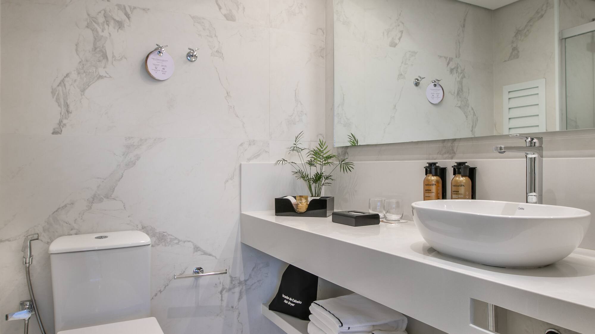 Modern white marble bathroom with vessel sink, toilet, and sleek vanity.