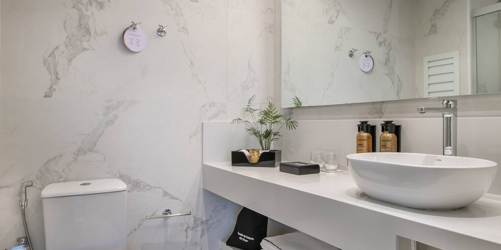 Modern white marble bathroom with vessel sink, toilet, and sleek vanity.