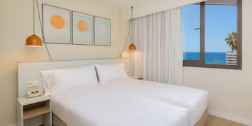 a bed with white sheets and pillows in a room with a window