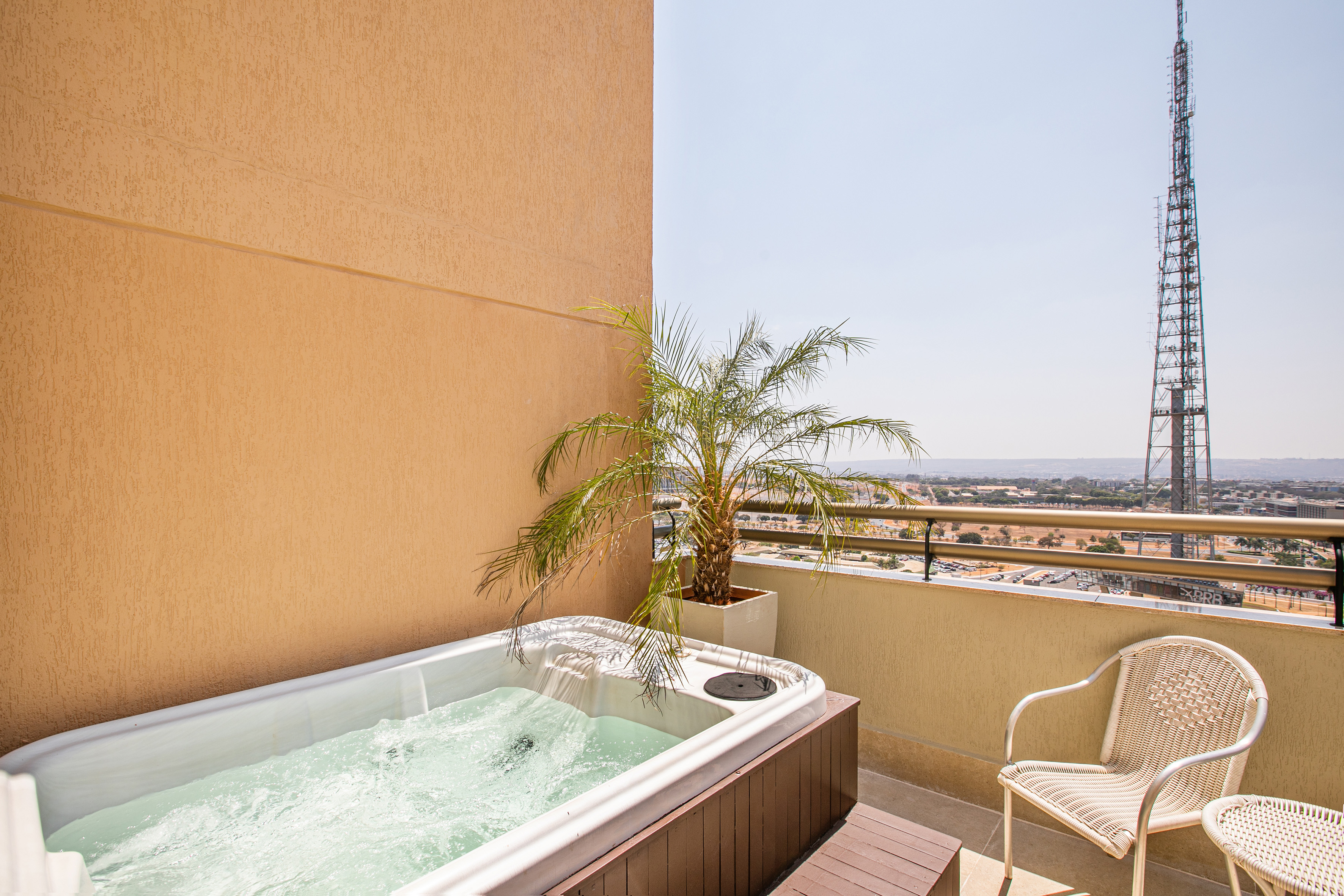 Rooftop balcony hot tub, palm tree, and city view with communication tower.