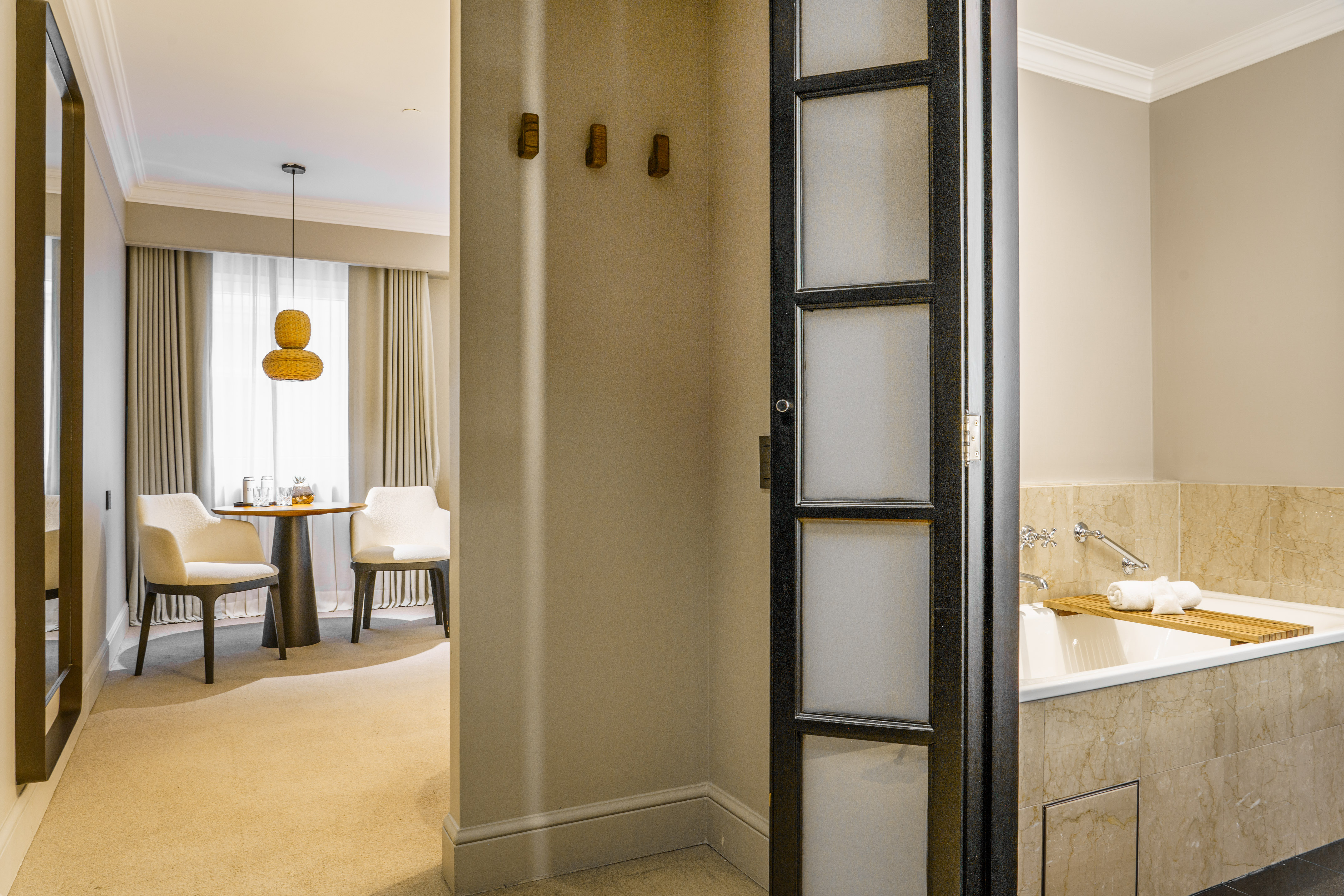 Hotel suite interior: modern seating area, adjacent bathroom with large tub.