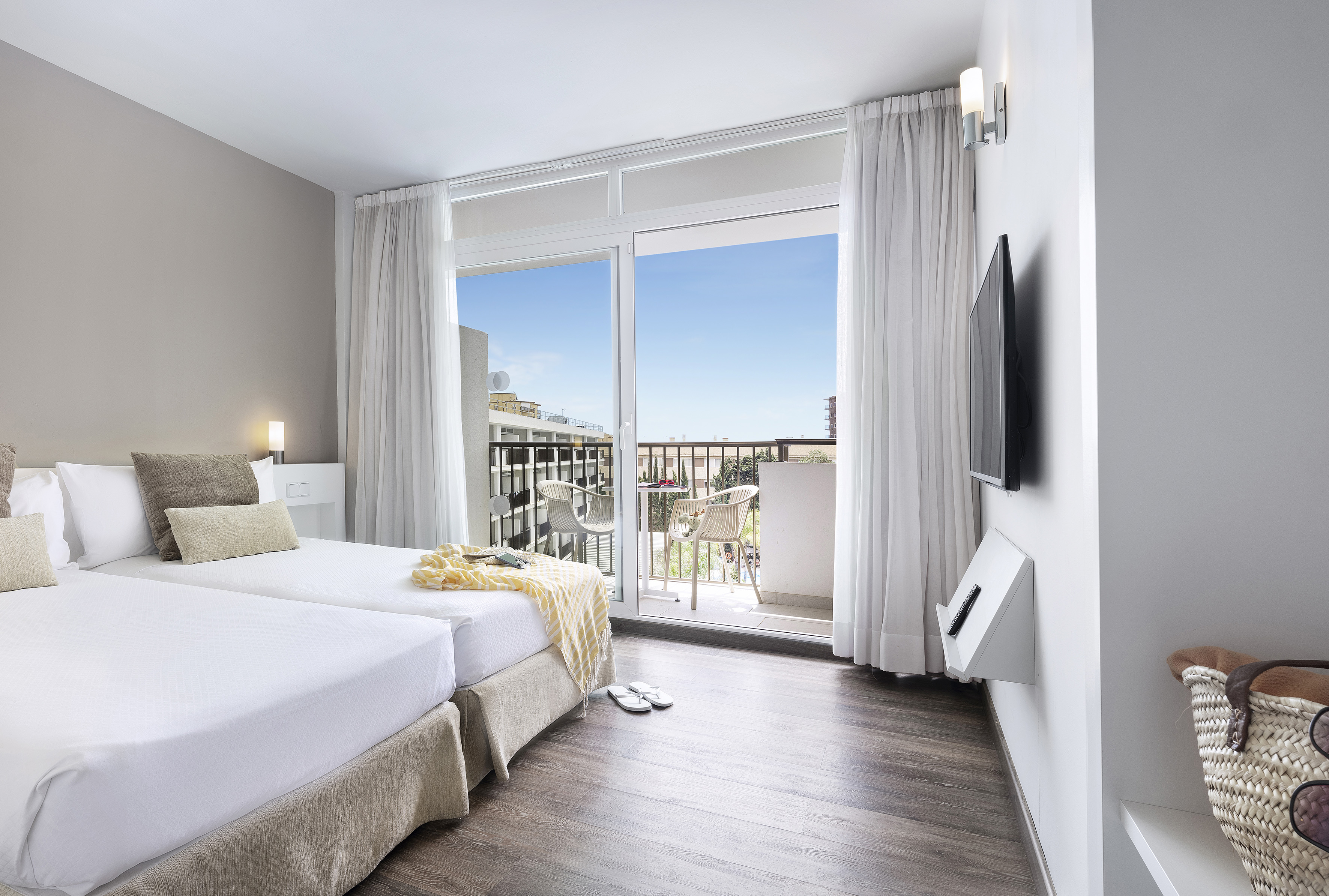 Modern hotel room with twin beds, bright decor, and balcony with seating.