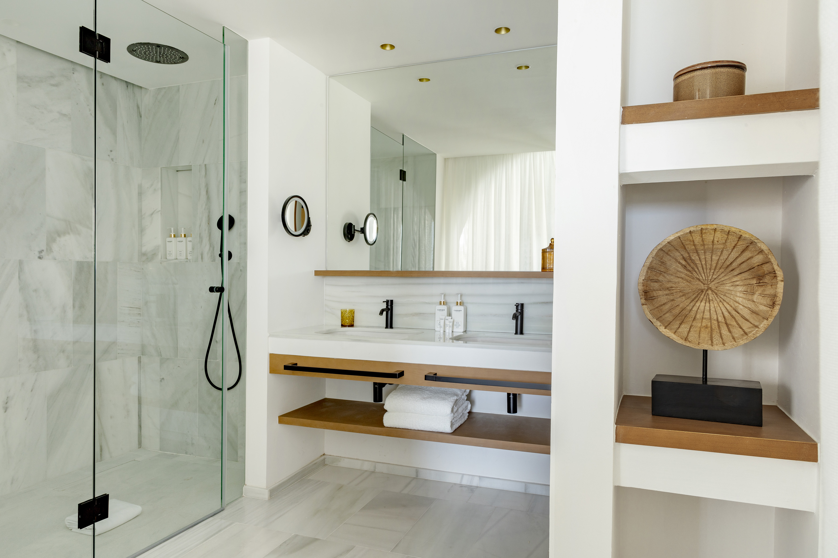 Modern bathroom with marble shower, double vanity, black fixtures, and wooden shelves.