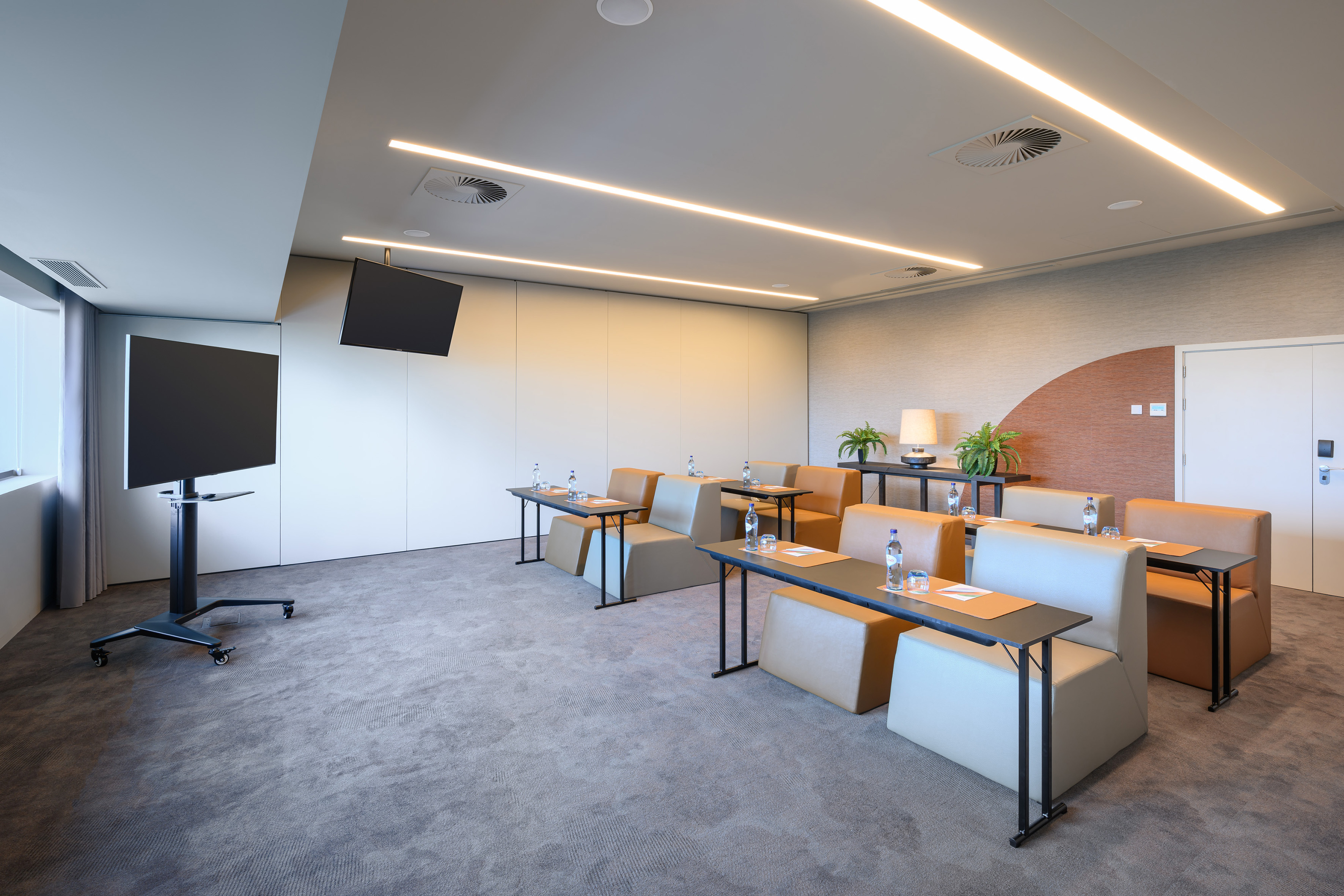 Modern conference room with comfortable seating, presentation displays, and linear lighting.