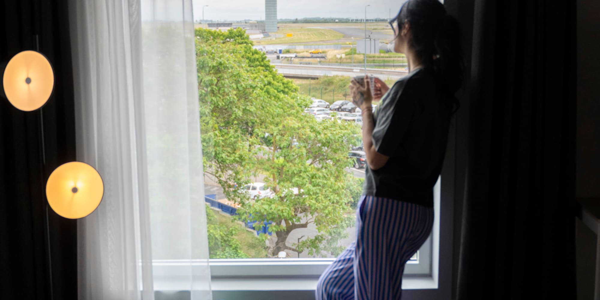 Traveler watching plane take off from modern airport hotel room.