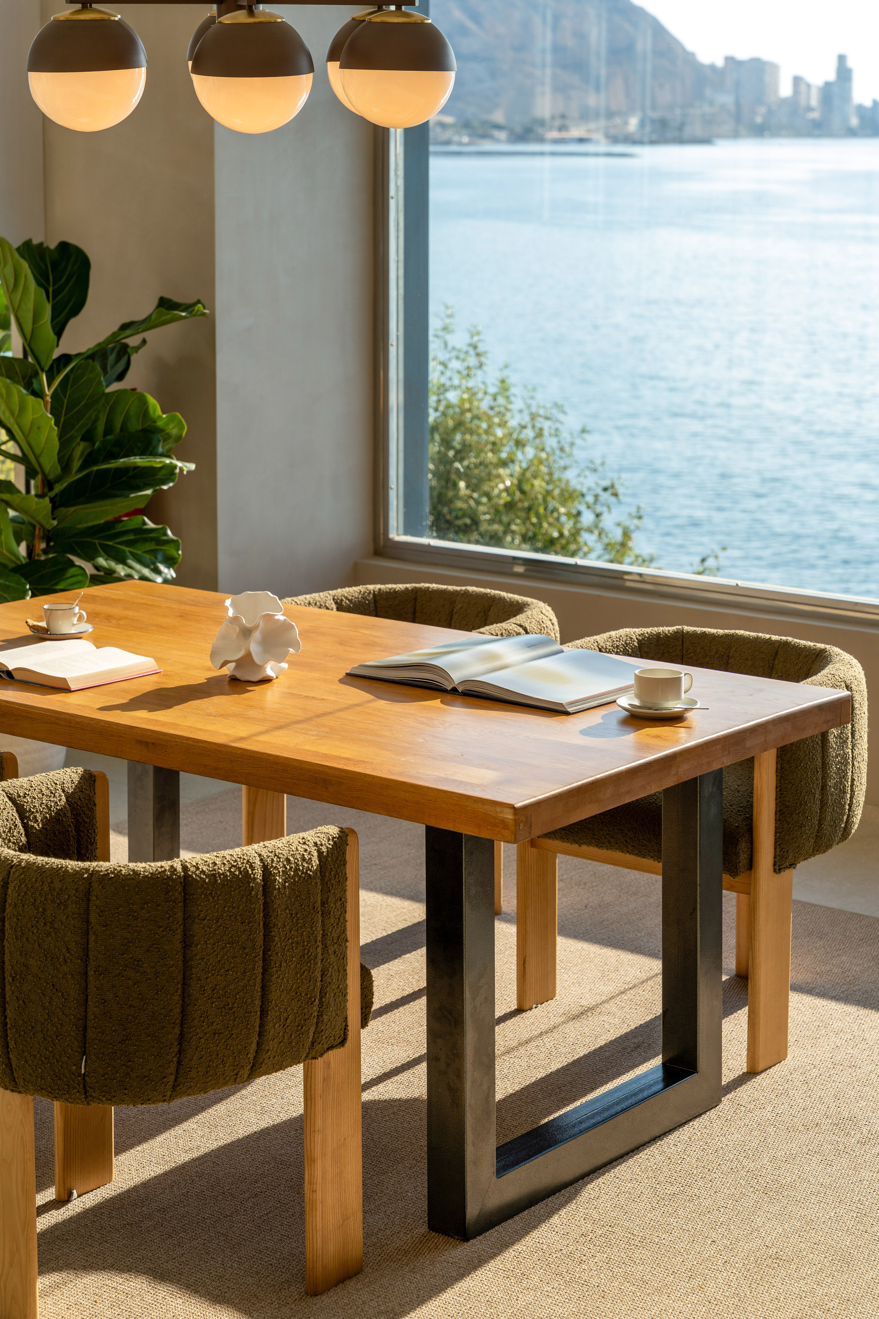 Modern dining room with wood table, green chairs, books, and ocean view.