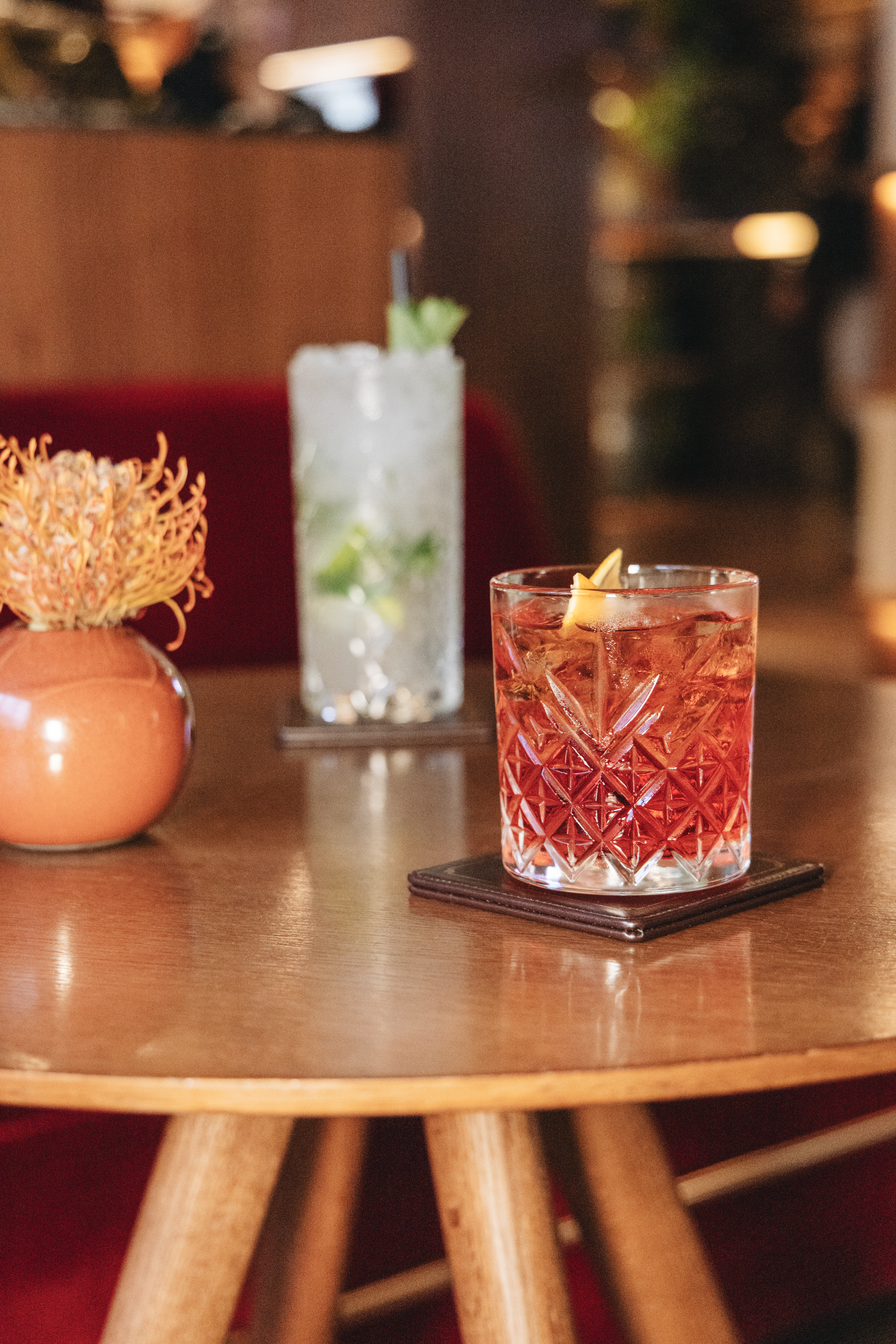 Classic red cocktail with orange peel on wooden table in a bar setting.