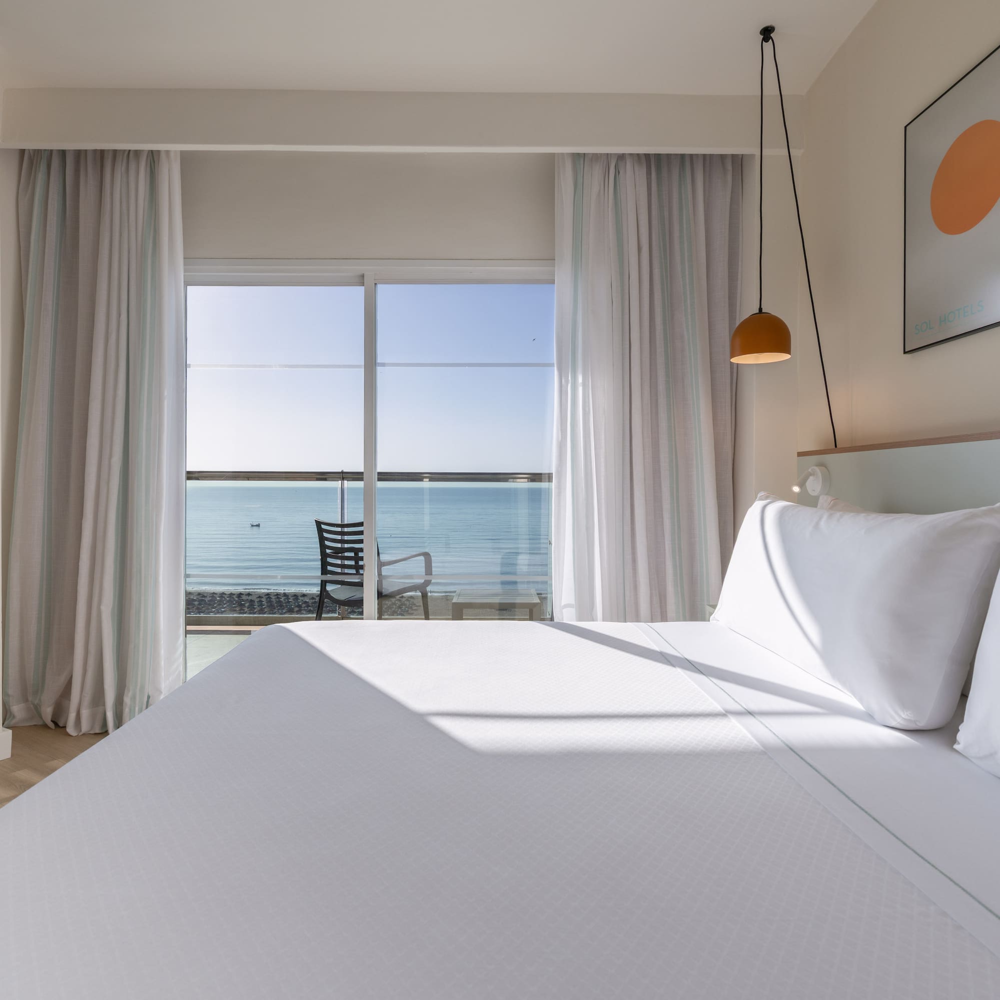 Modern hotel room with white bed, ocean view balcony. Sol Hotels branding.