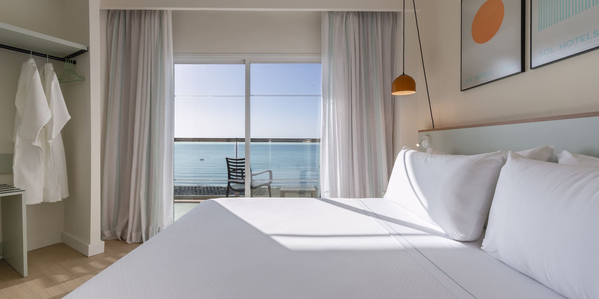 Modern hotel room with sea view, balcony, white bed, and Sol Hotels branding.