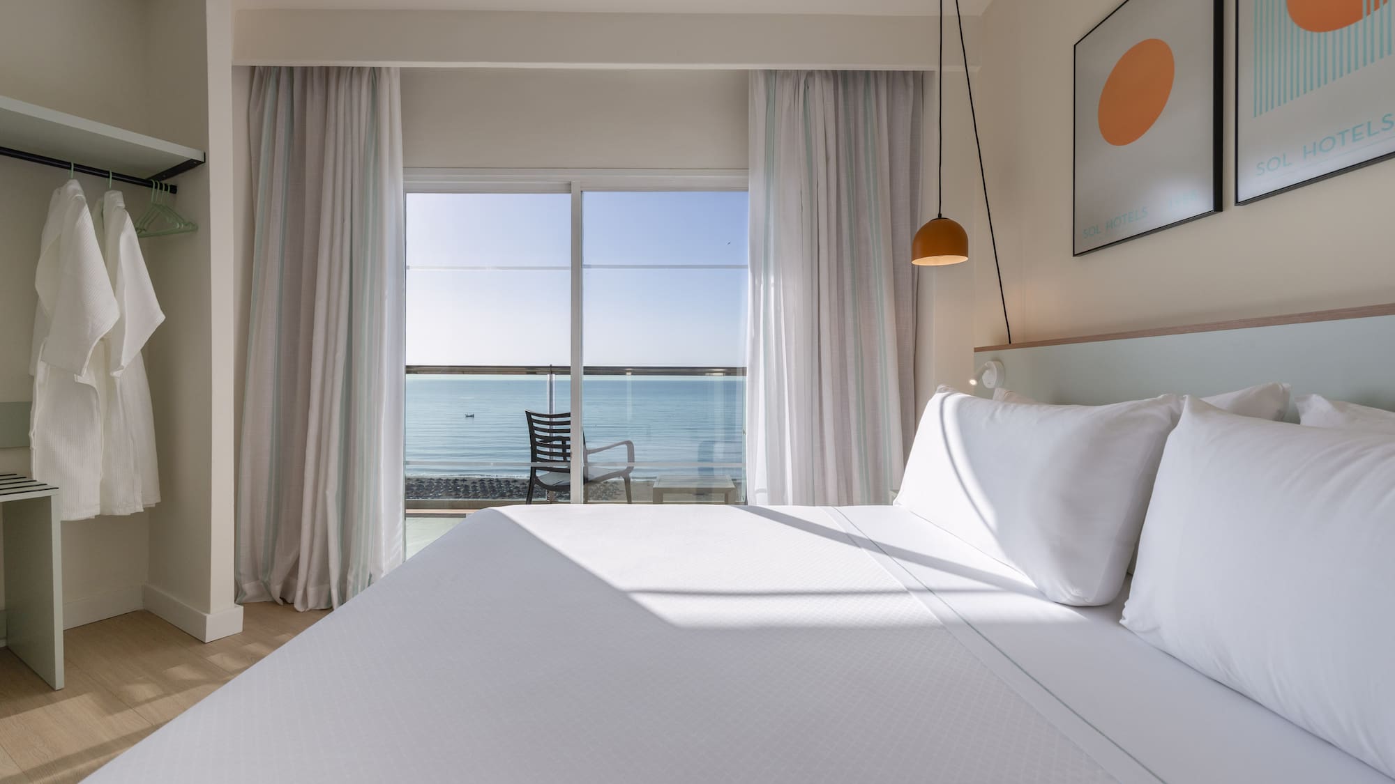 Modern hotel room with white bed, ocean view balcony. Sol Hotels branding.