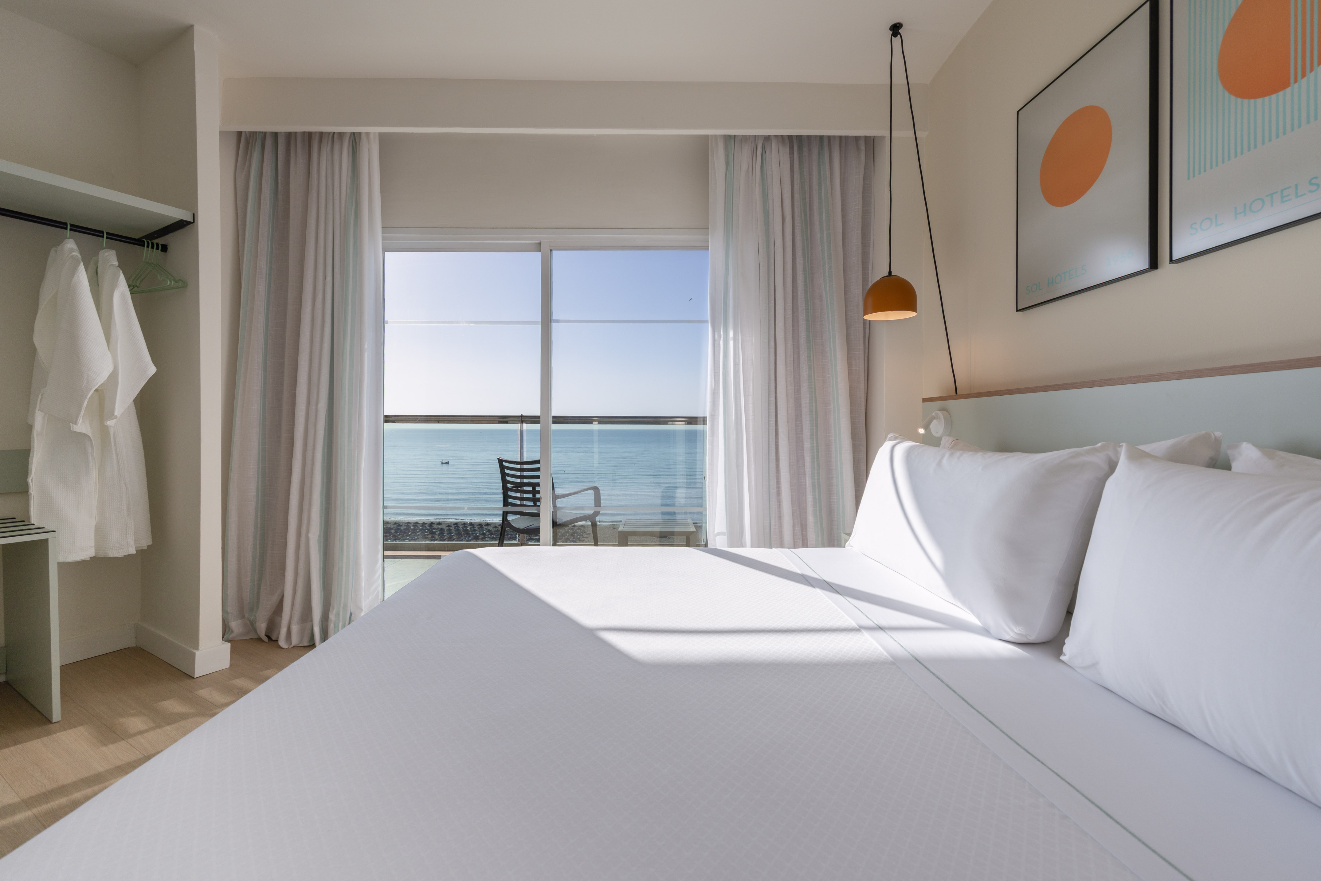 Coastal hotel room with white bed, balcony, and panoramic sea view.